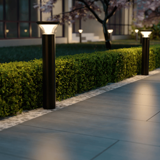 Modern pathway with sleek black bollard lights illuminating tiled walkway and neatly trimmed hedges at night.