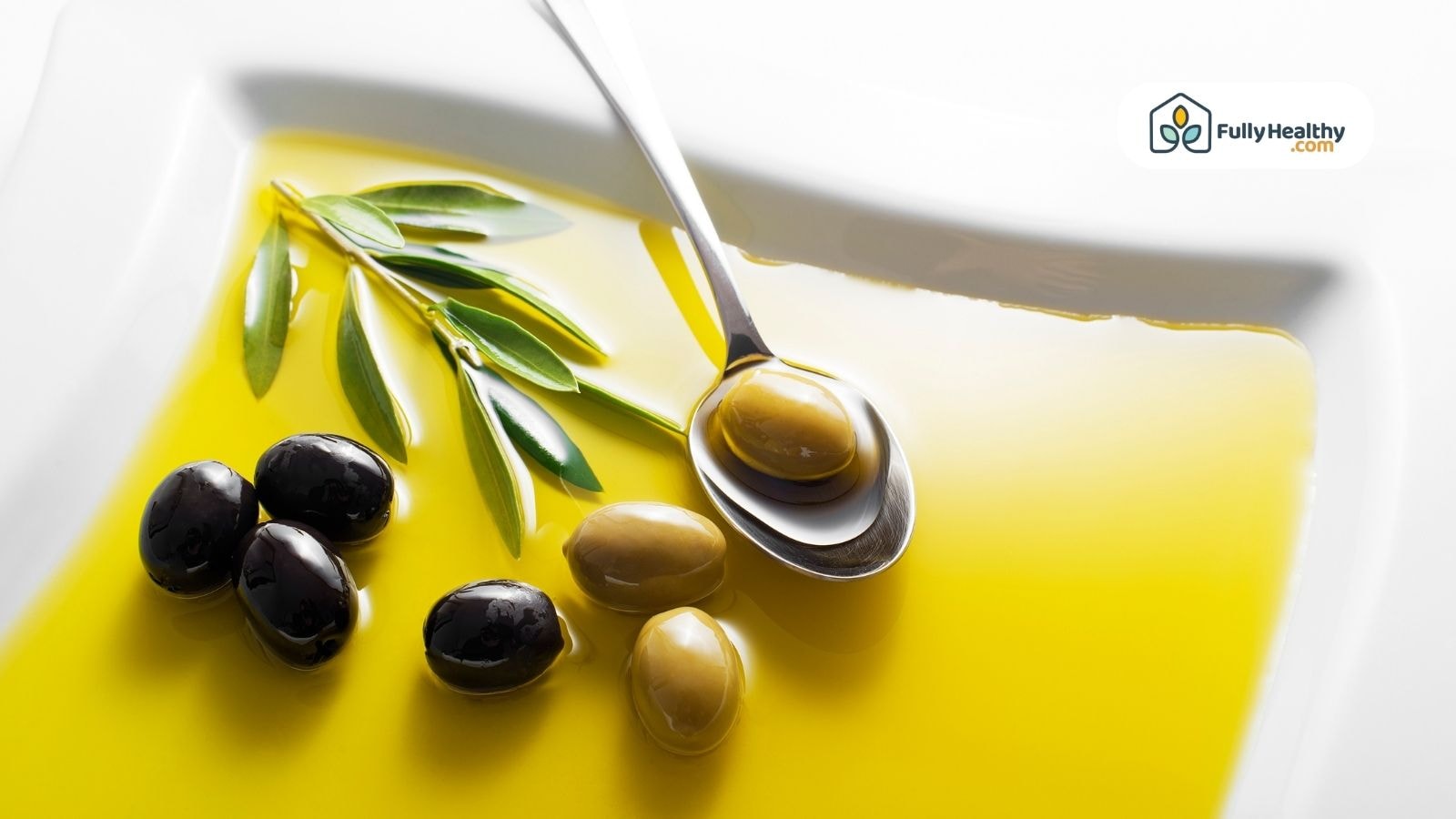 Spoon of olive oil on a plate with black and green olives and olive leaves.