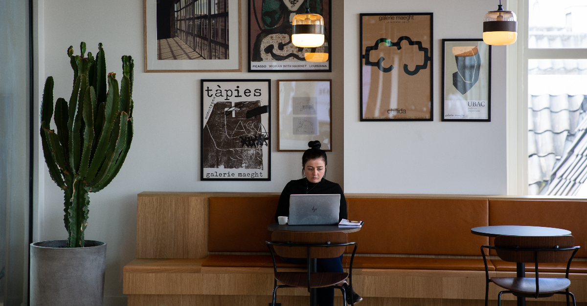 Vrouw zit alleen op een bank en werk aan een cafetafel met haar laptop.