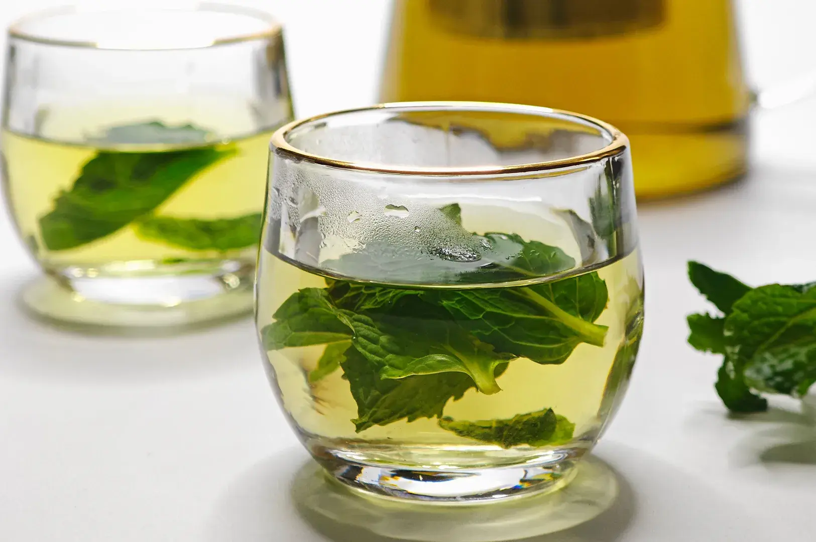 Clear gold-rimmed glasses filled with fresh mint tea on a white background.