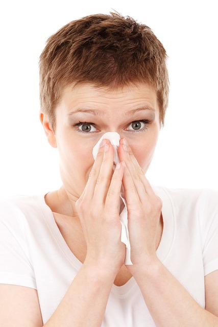 An image of a woman with a common cold blowing her nose into a tissue. 