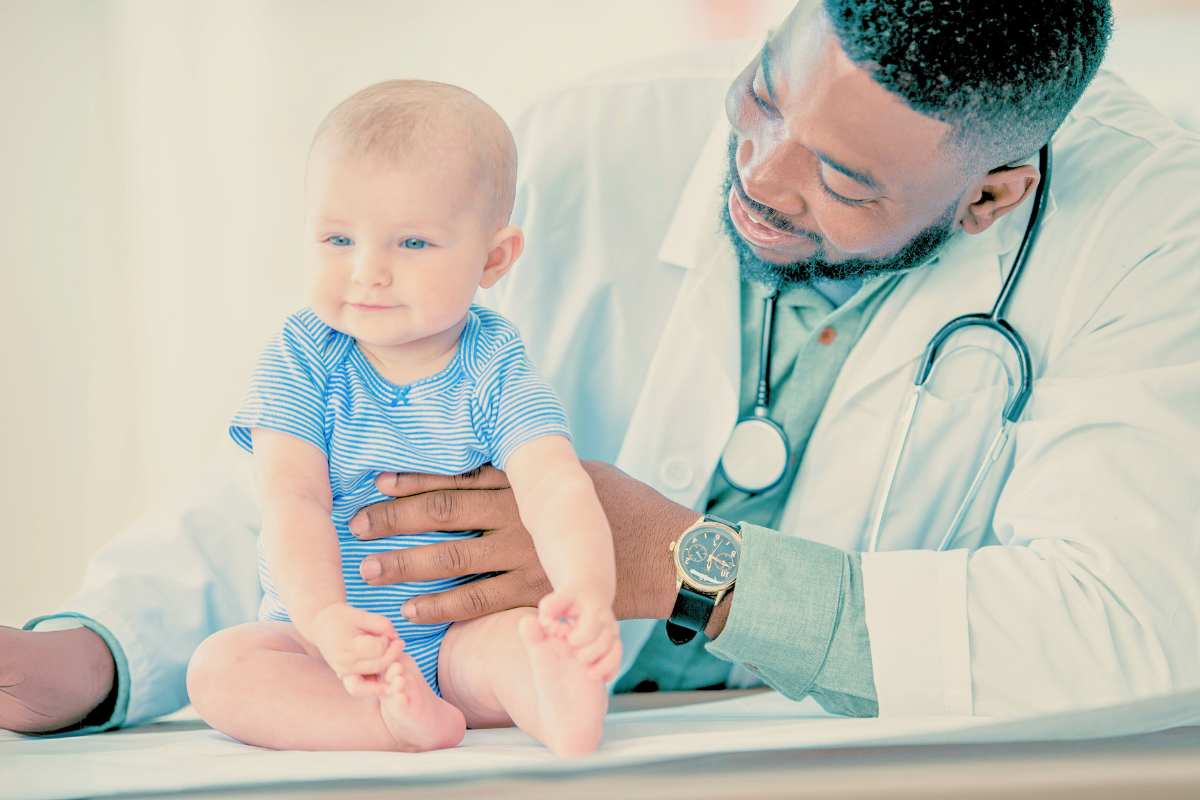 Baby sitting up next to doctor. Poppyseed Play