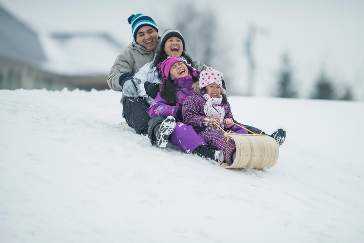 Happy family of four sledding down a hill. 