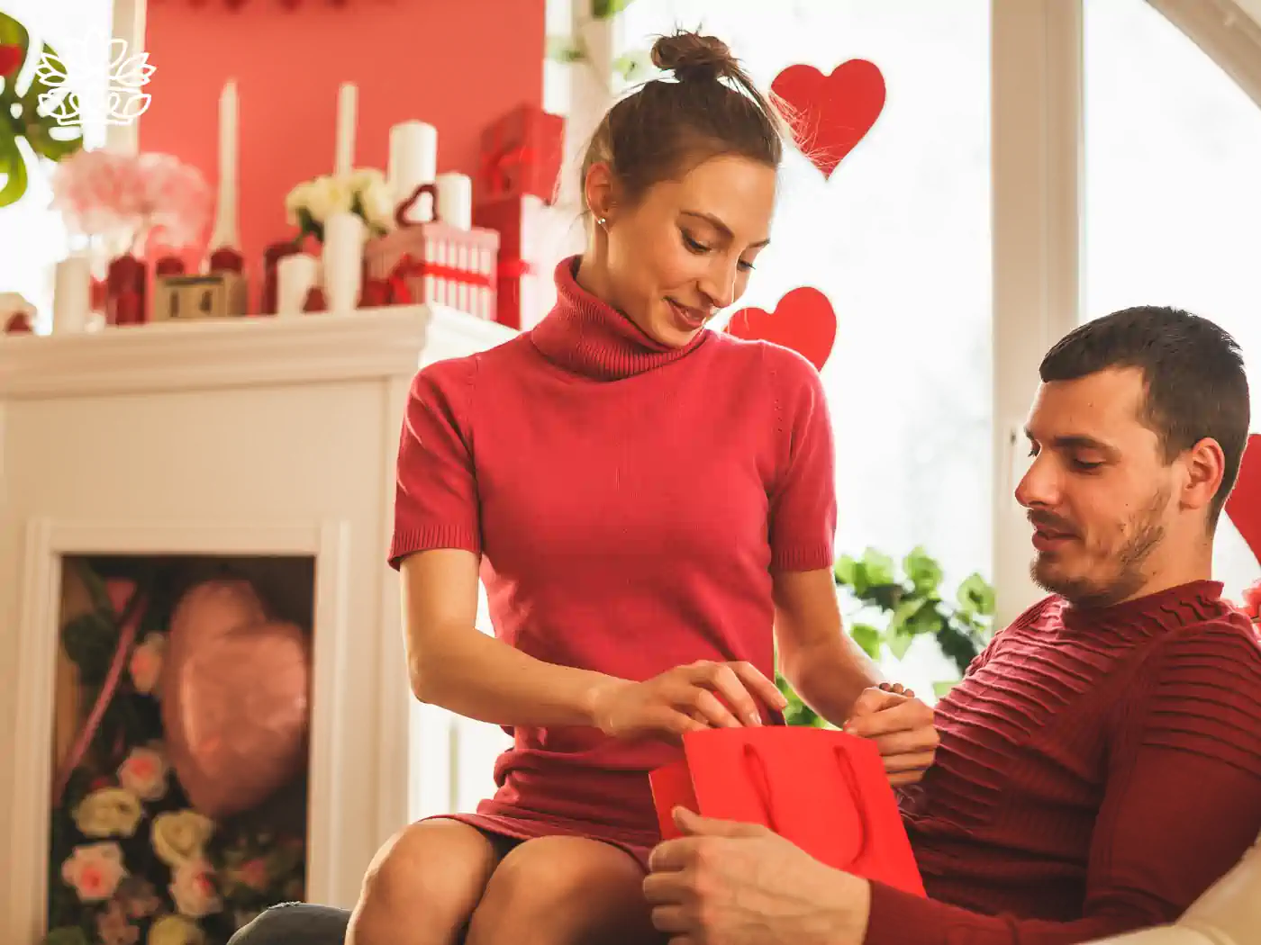 Woman in red sweater giving a Valentine's Day gift to a man in a cozy, heart-decorated living room. Fabulous Flowers and Gifts