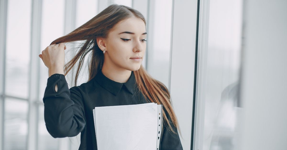 Woman holding fidelity tax documents while adjusting her hair in a bright office space.