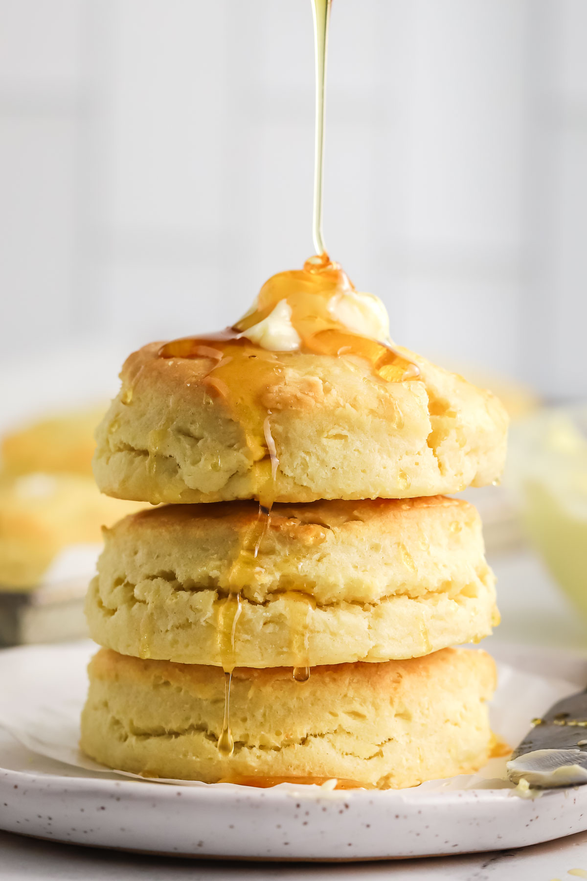 three cream biscuits stacked on a plate topped with butter and drizzled with honey