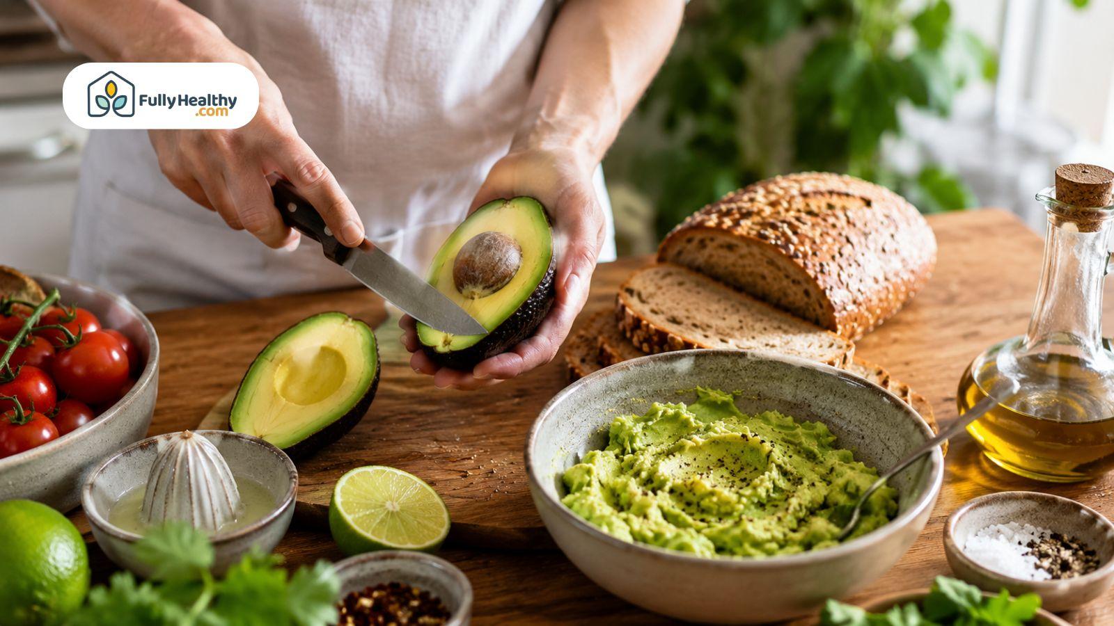 Person slicing avocado beside mashed avocado and fresh healthy ingredients