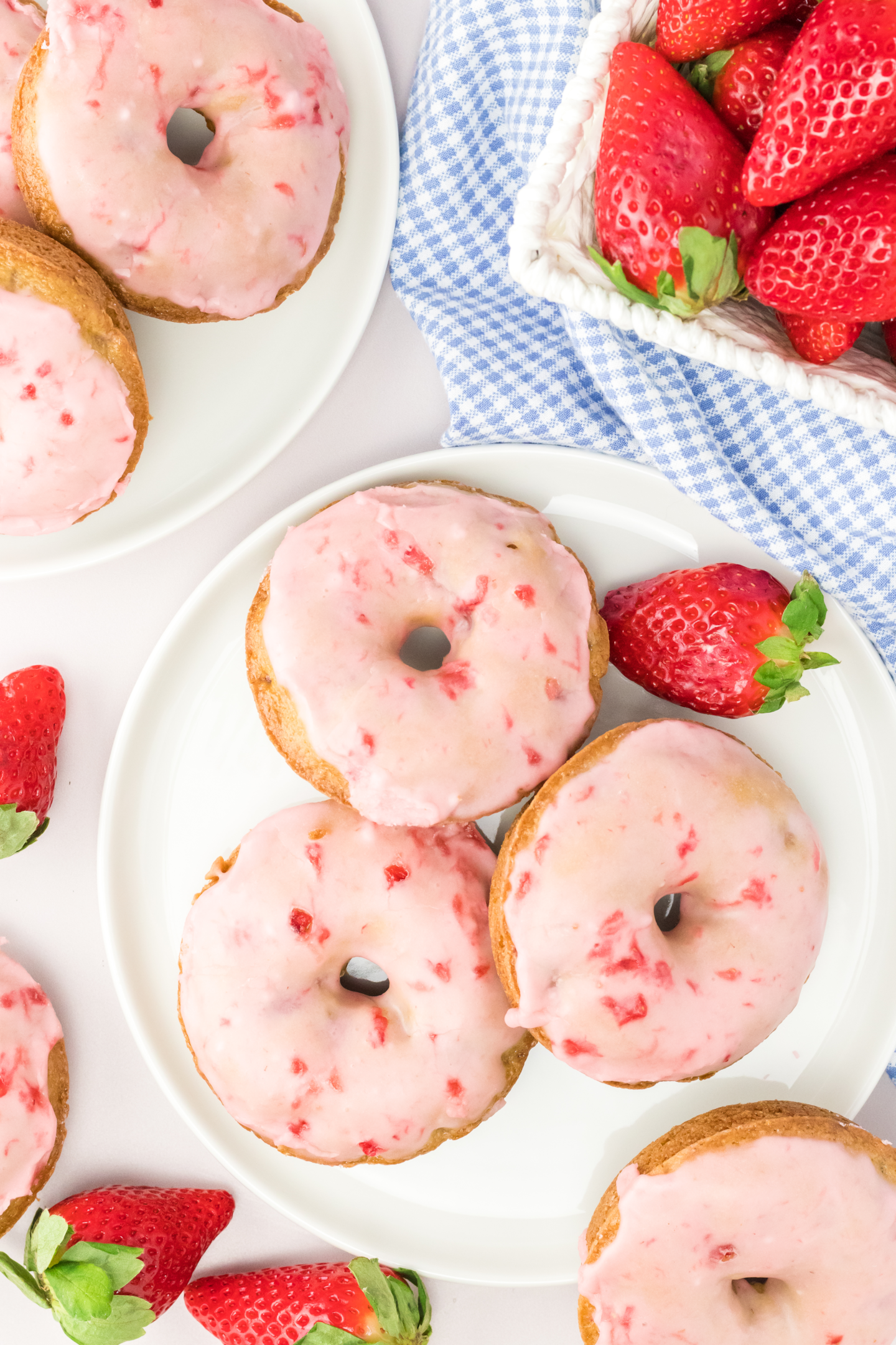 three baked strawberry donuts topped with strawberry glaze on a plate