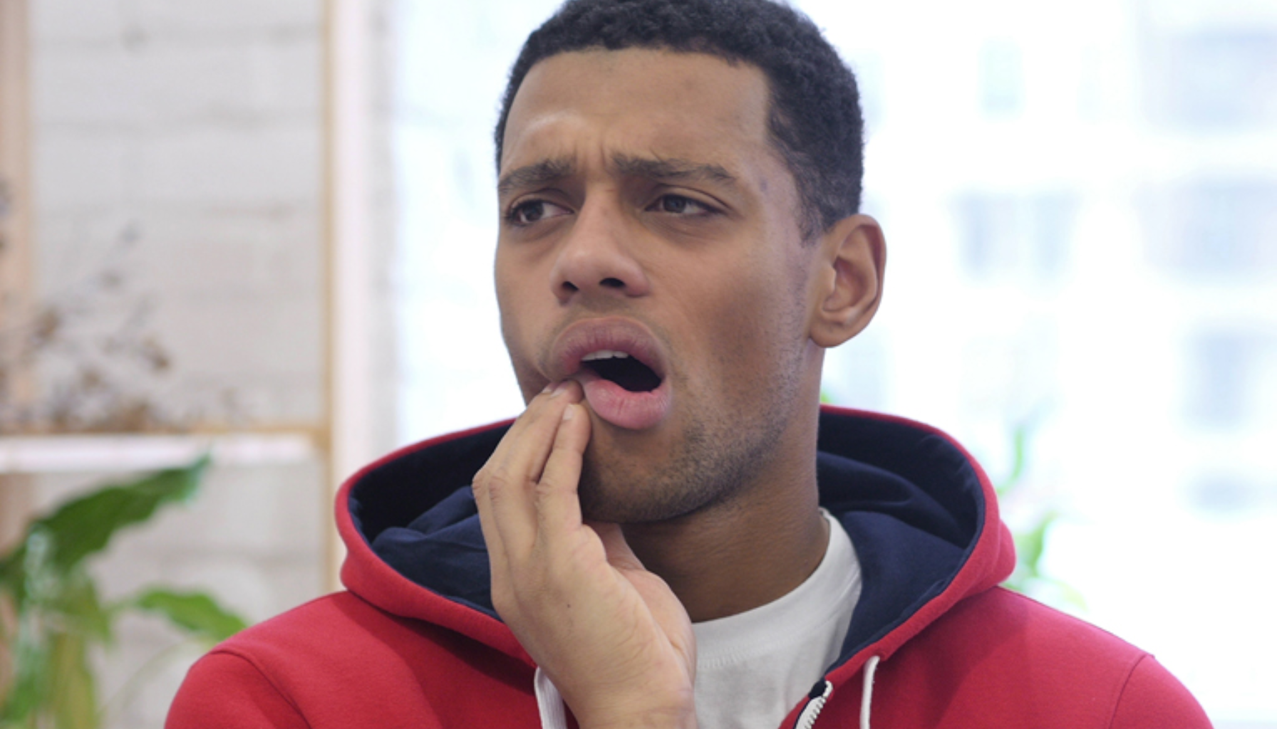 Mann med smertefullt uttrykk holder hånden mot kjeven, tydelig plaget av tannverk eller munnrelatert ubehag.