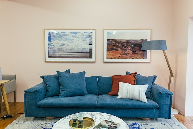 low blue fabric sofa with a floor lamp and two wall art pieces - image credit: https://www.pexels.com/photo/soft-couch-with-cushions-in-spacious-living-room-4857772/