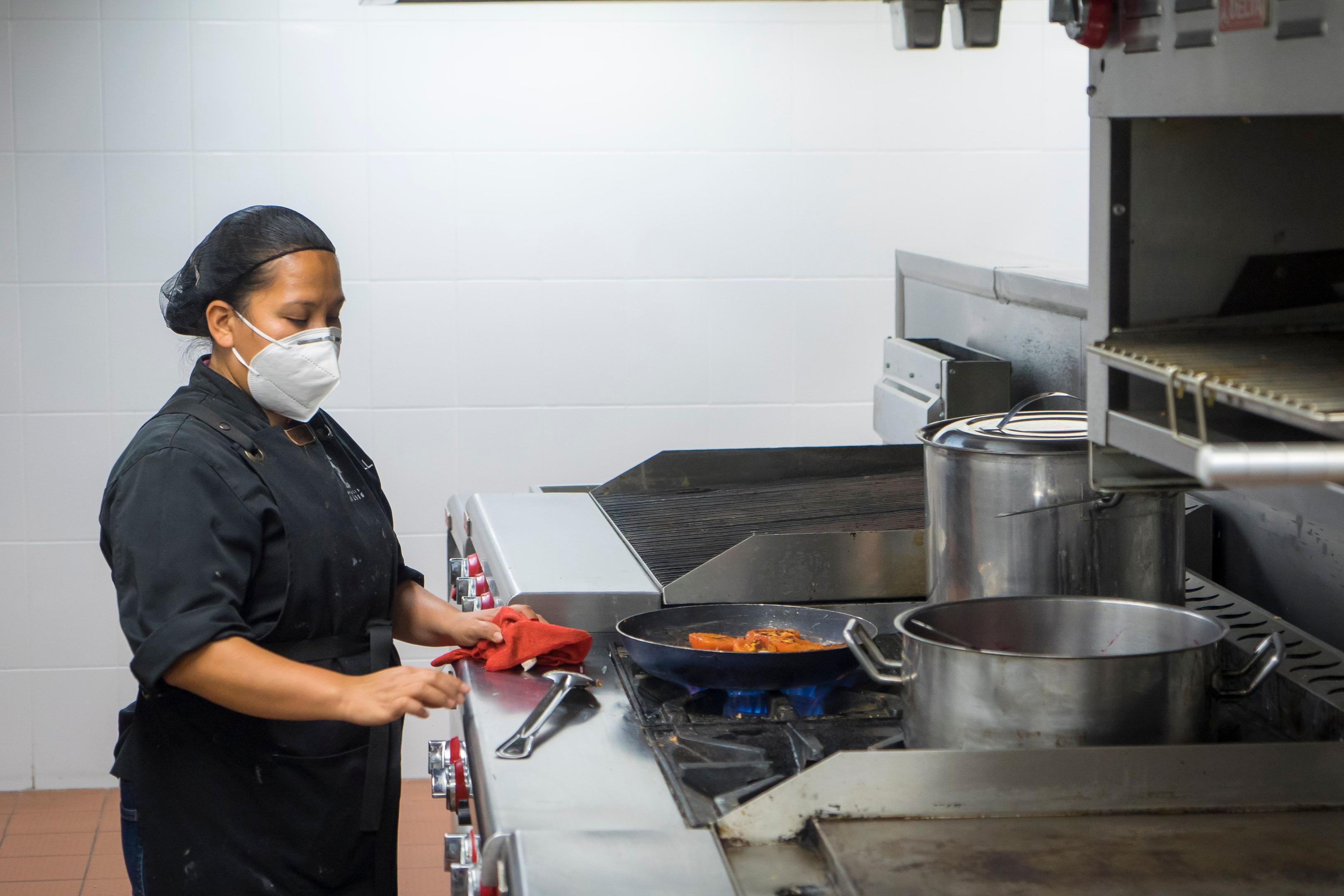 A chef in a busy commercial kitchen is meticulously portioning fresh ingredients on a prep station, showcasing attention to detail that is crucial for managing restaurant food costs and ensuring consistent plate cost. The organized workspace reflects the importance of inventory management and proper training in maintaining efficiency in the restaurant industry.