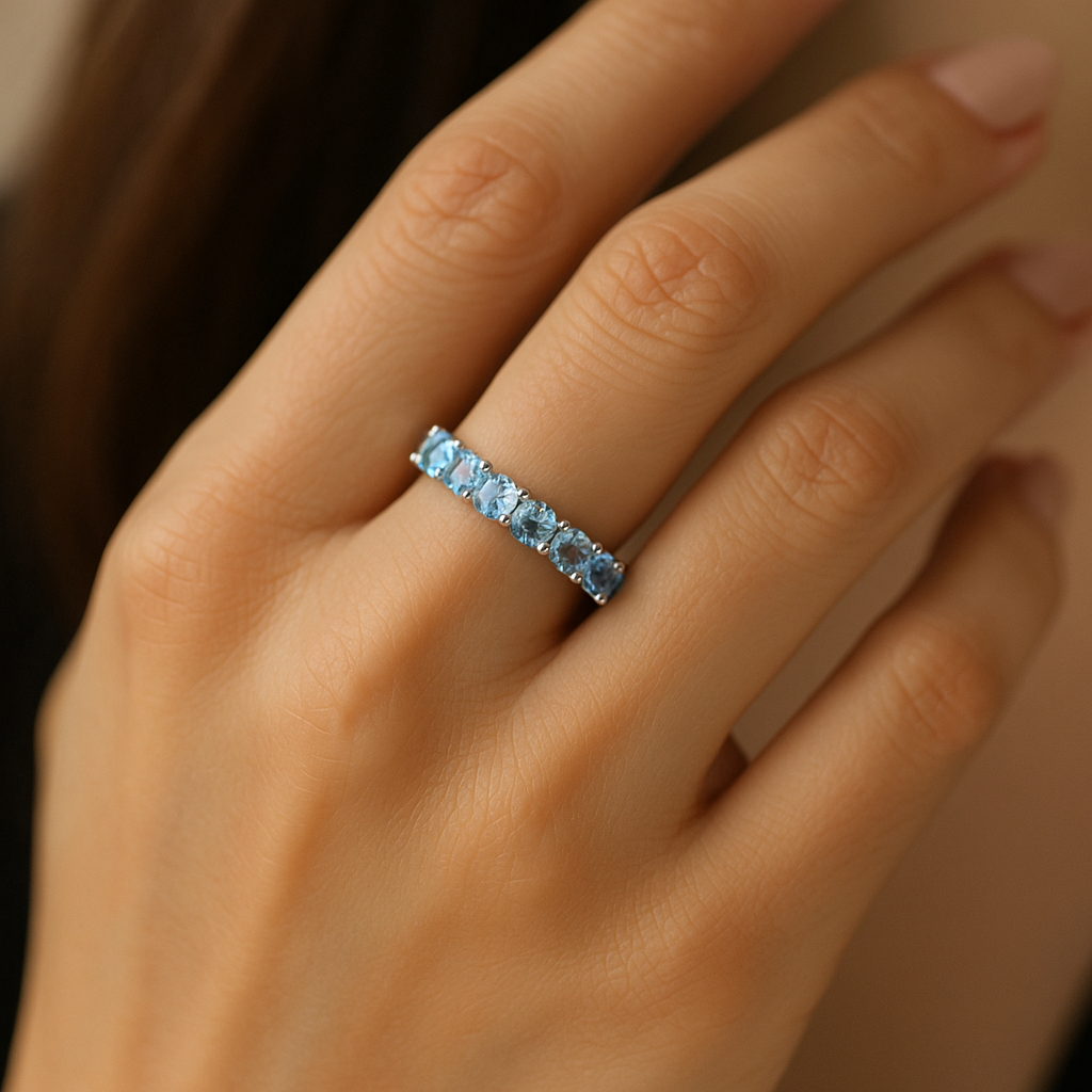 Stilingos moters ranka su žiedu juostele iš balto aukso, inkrustuotu šviesiai mėlynais akvamarinais ir deimantais, atspindinčiais vandens žvilgesį