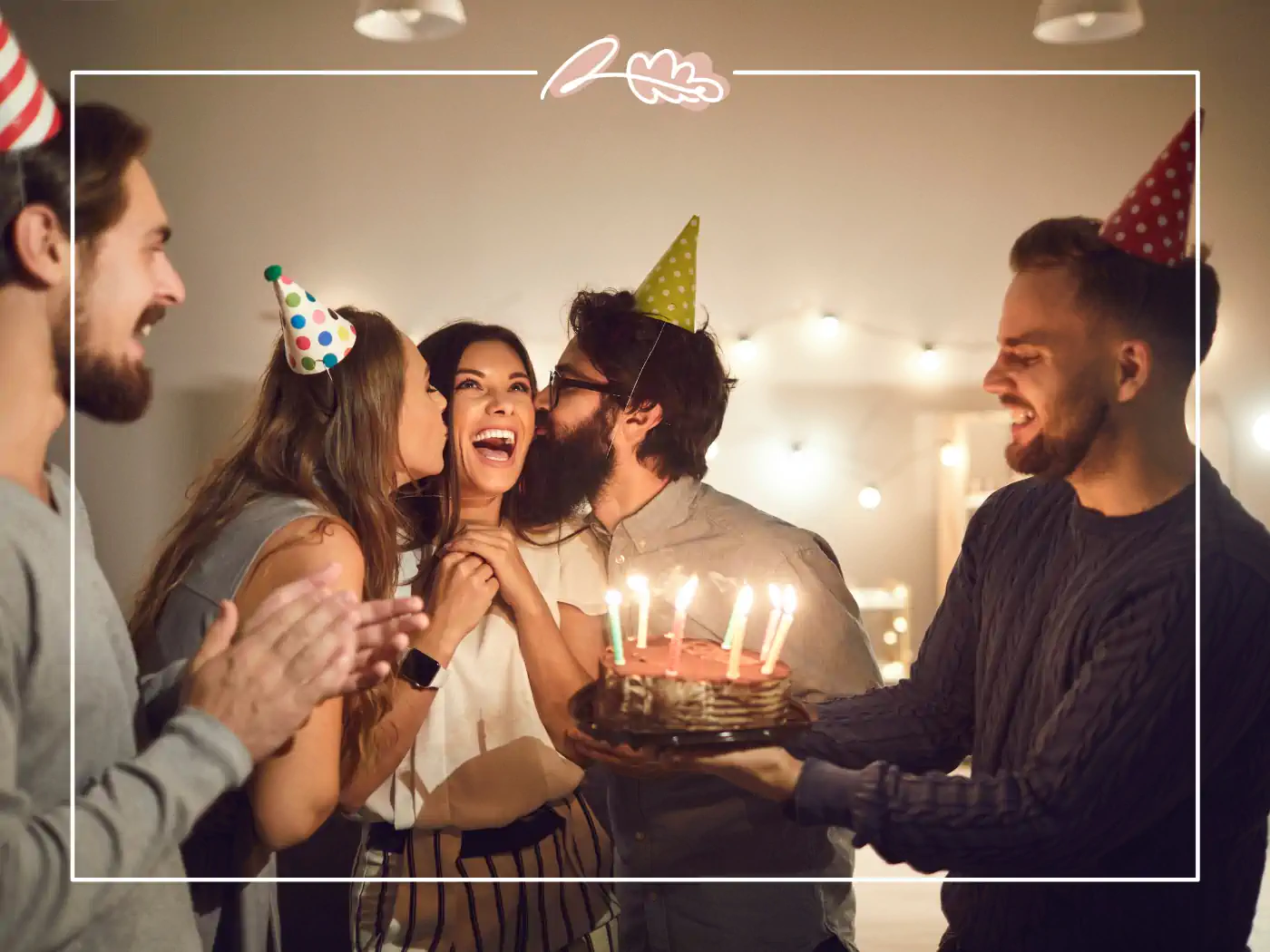 A joyful group of friends celebrating a birthday, with one holding a chocolate cake with lit candles and others clapping and smiling in a warmly lit room. Fabulous Flowers and Gifts.