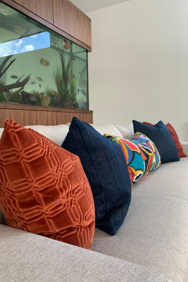 a series of plush pillows on a beige couch with a fish tank behind them