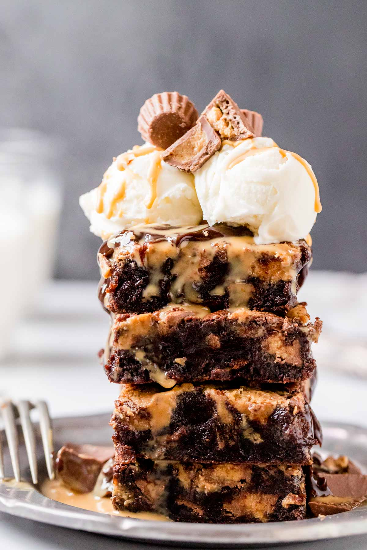 four peanut butter swirl brownies stacked on a plate topped with ice cream, and a peanut butter cup