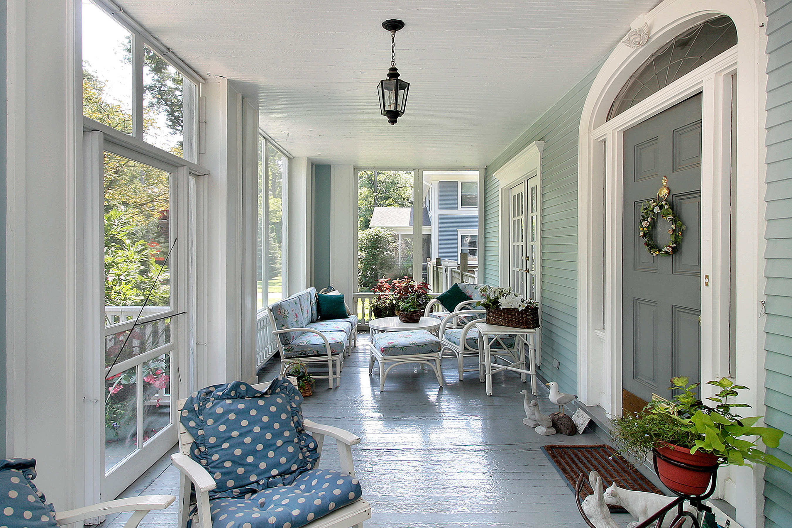 Front porch seating area in front of a blue home with protective screens.