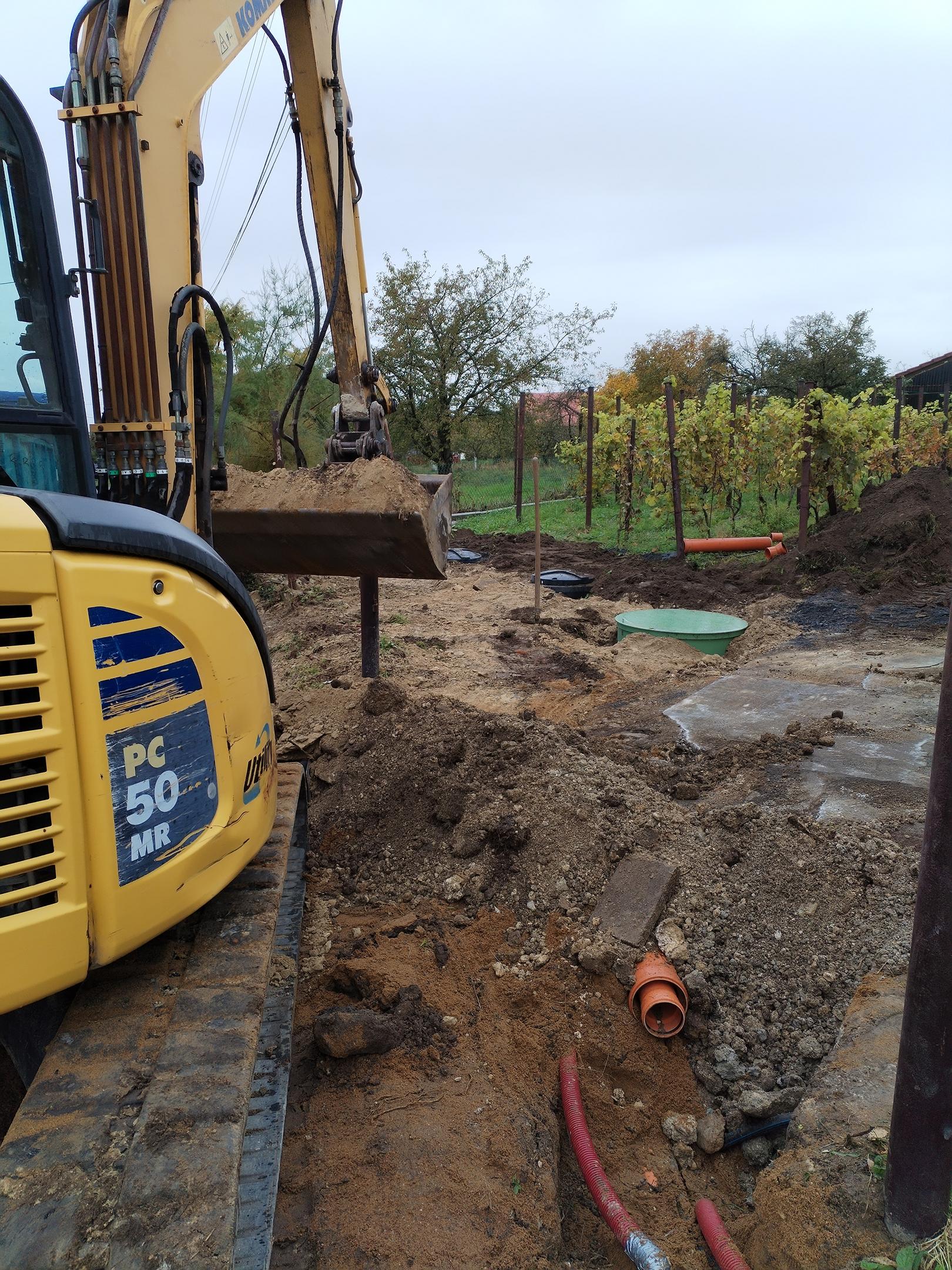 Zemní práce při instalaci domovní ČOV na klíč, bagr, usazená čistírna a kanalizační potrubí na zahradě.