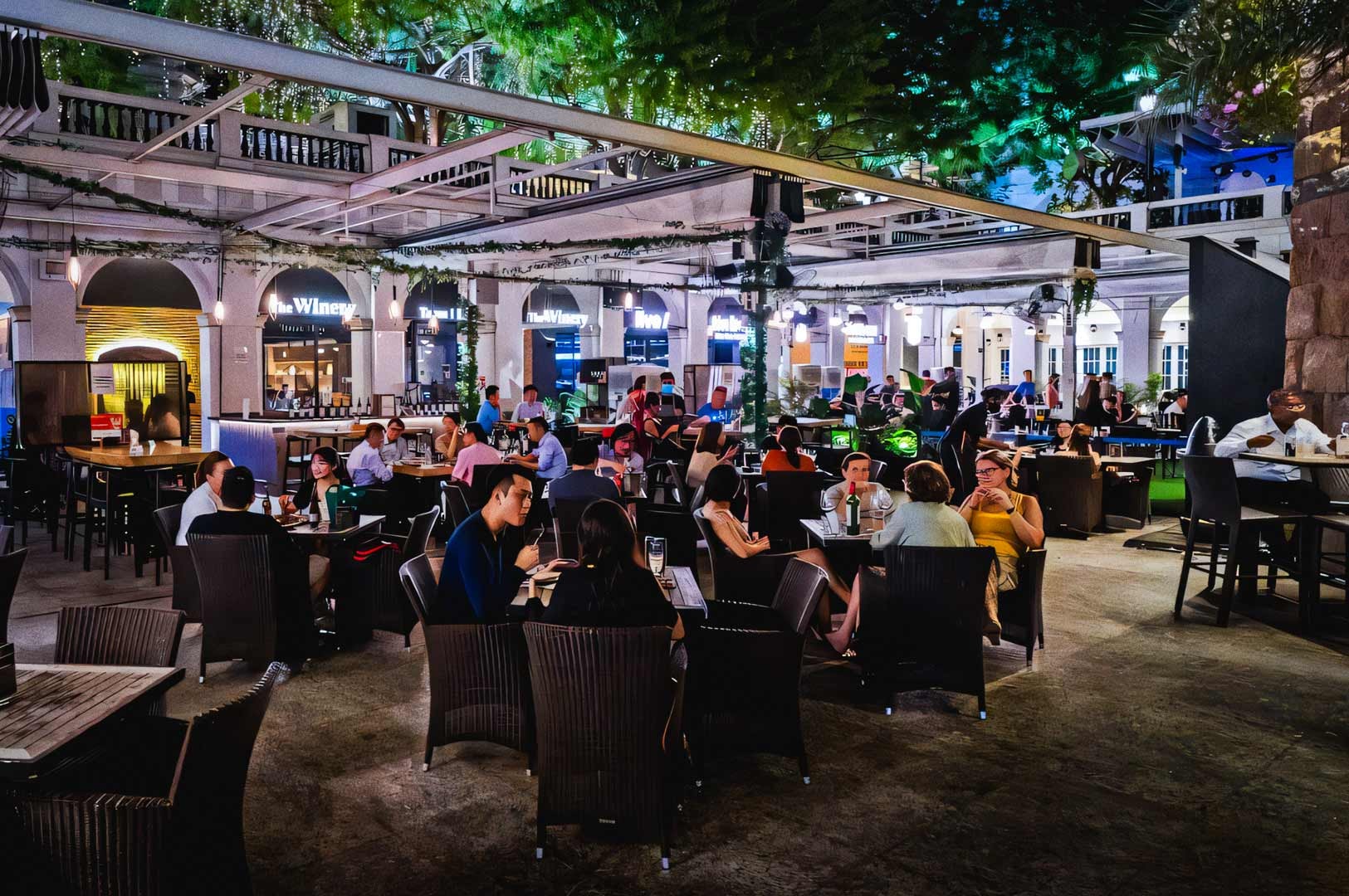 Outdoor dining area at CHIJMES with lively crowds, illuminated bar façades, and a vibrant night atmosphere under open-air canopies.