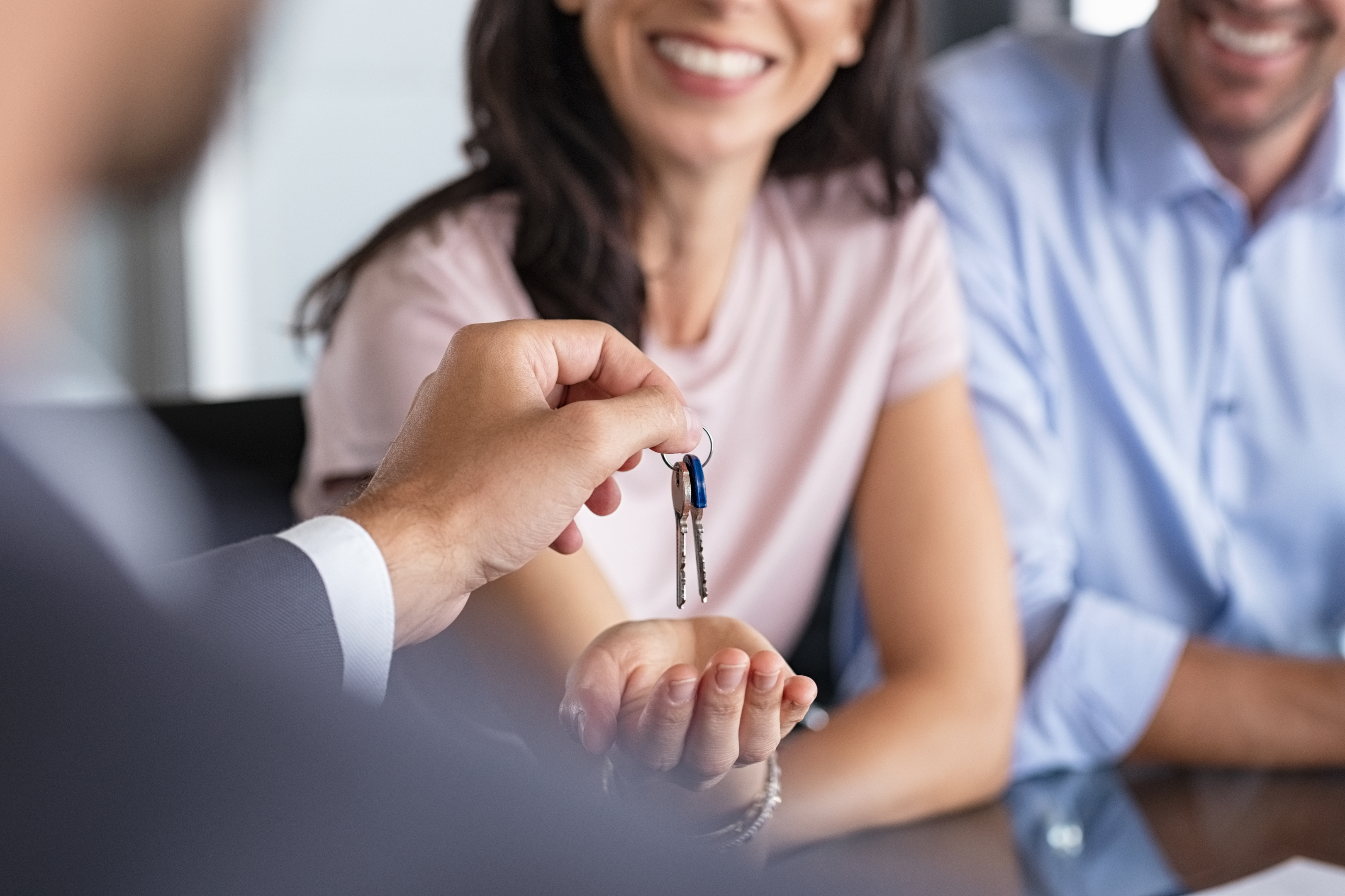 Immobilienmakler übergibt Frau und Mann Schlüssel zu Ihrer Traumwohnung.