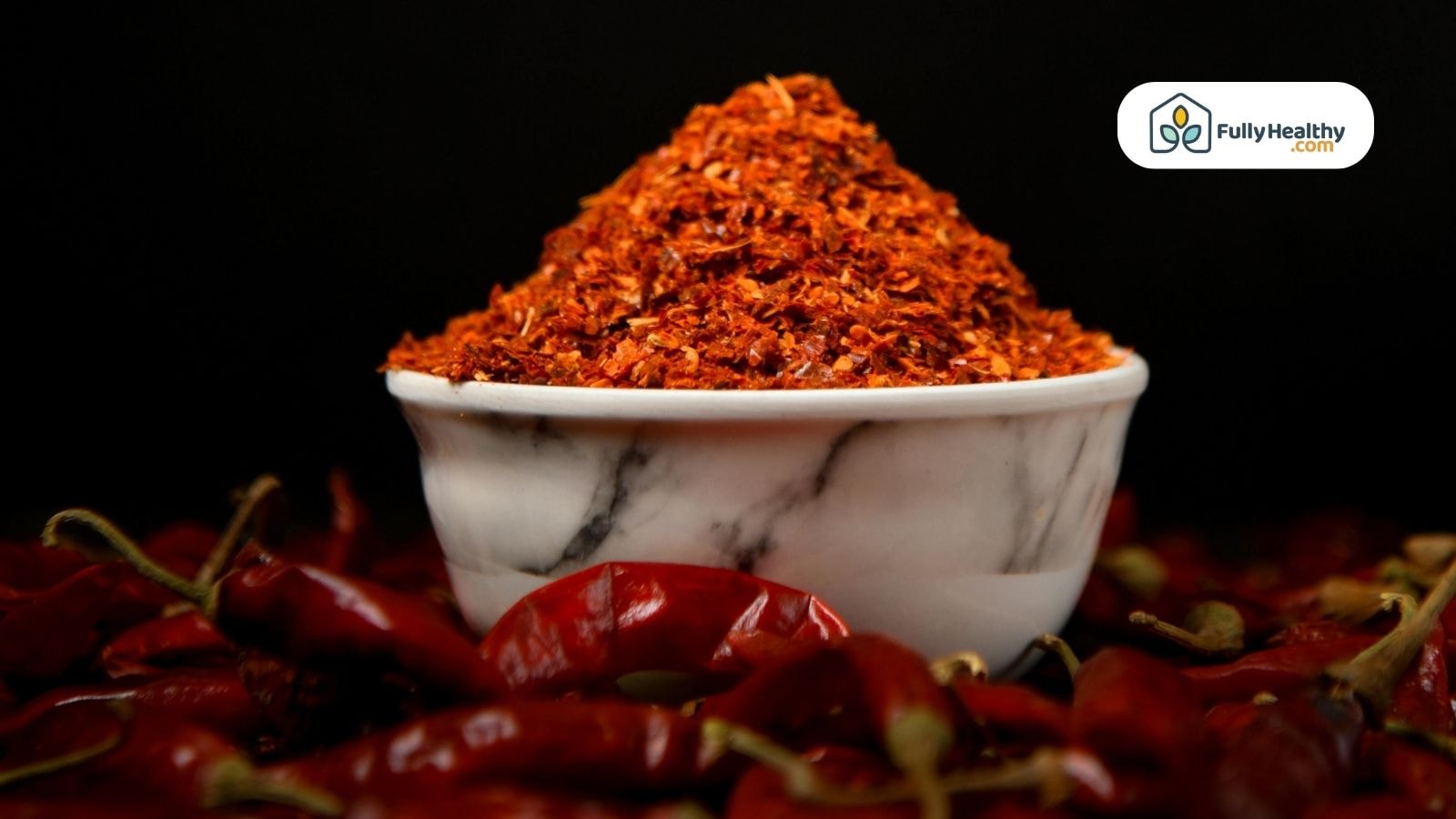 A close-up of a bowl filled with ground chili pepper powder surrounded by dried chilies
