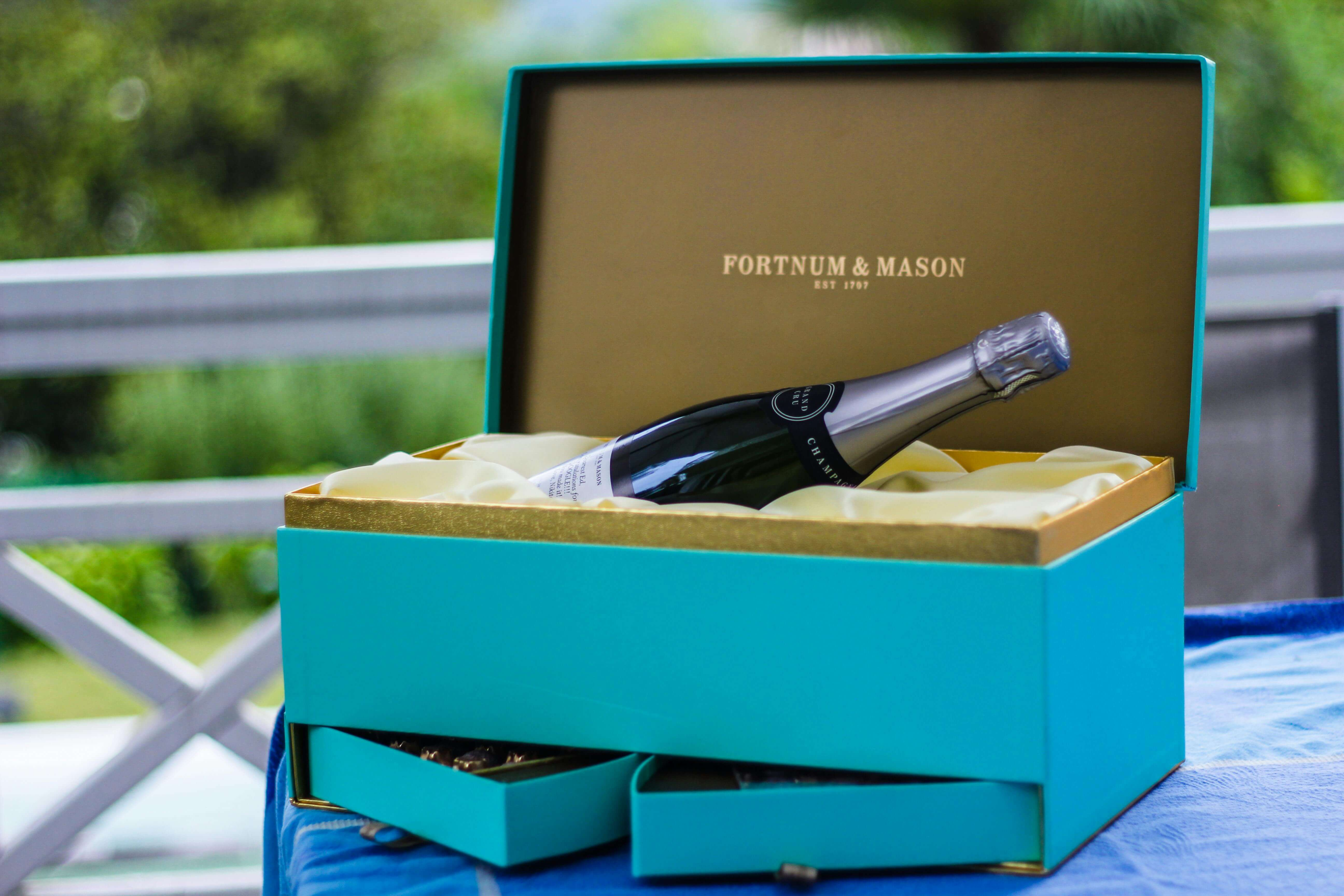 Turquoise gift box with champagne and chocolates, open on an outdoor table.