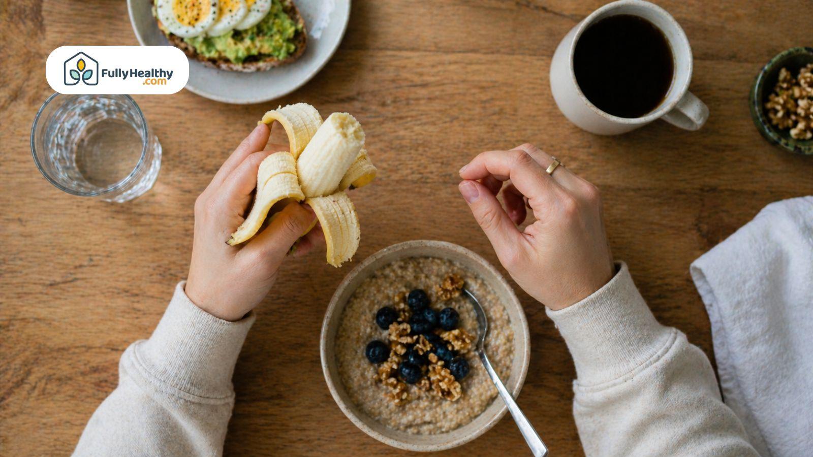 Person holding and peeling a banana above a bowl of oatmeal with blueberries and granola.