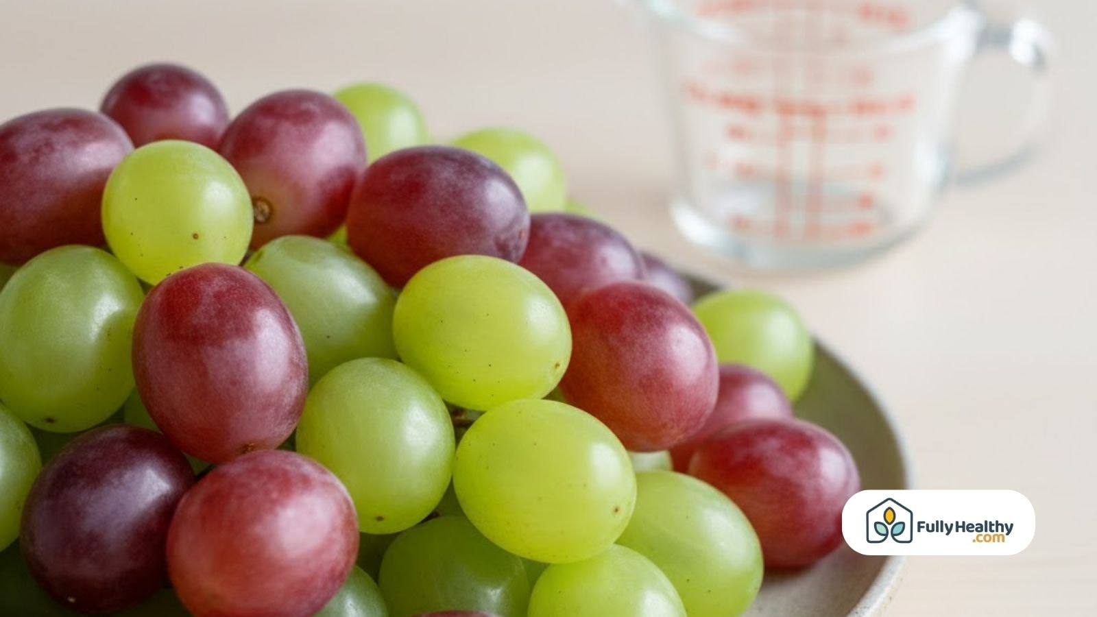 Red and green grapes shown in a bowl with a measuring cup.