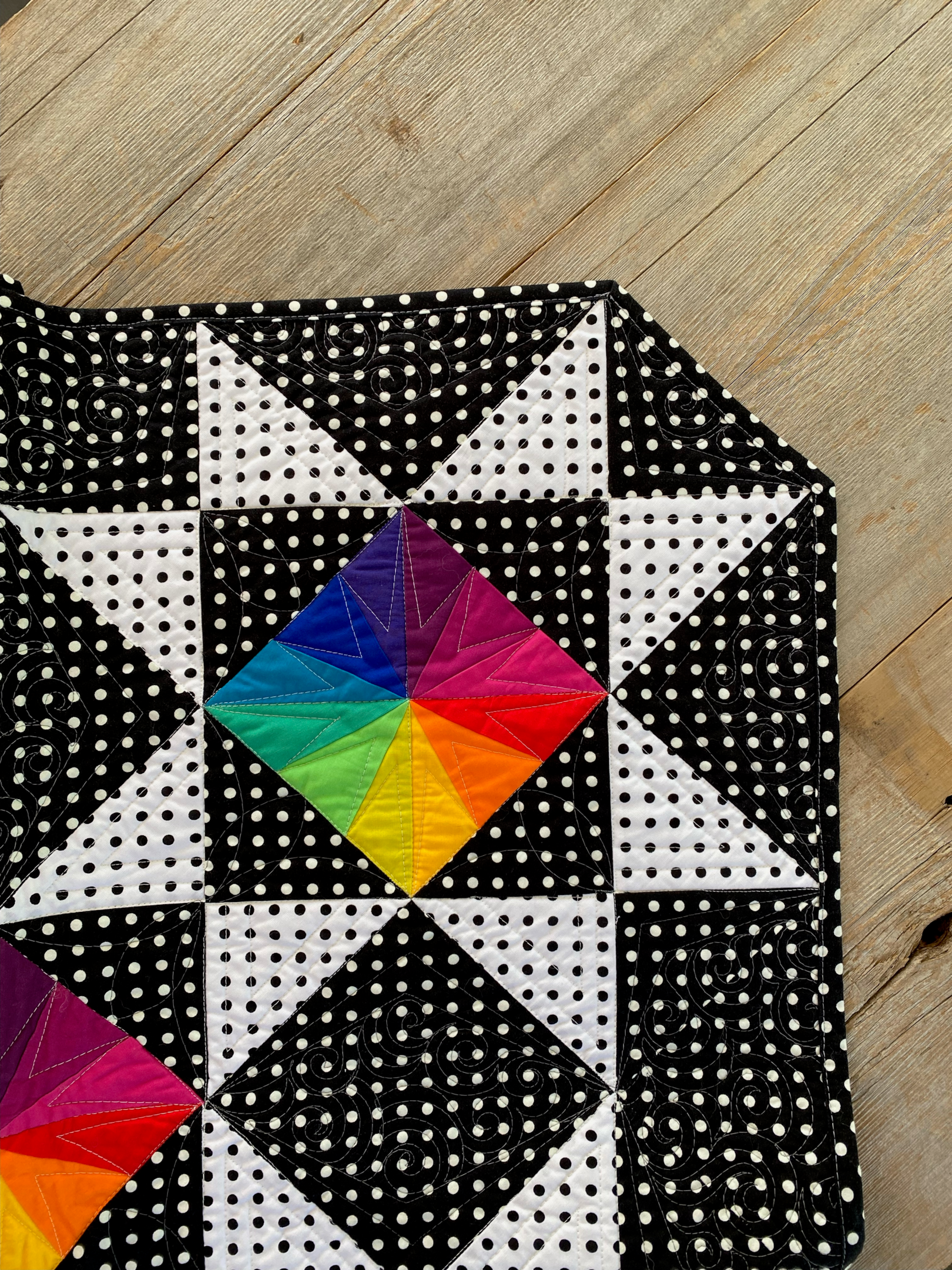 Lucy in the Sky quilt pattern with a black and white print binding paired with rainbow colored blocks.
