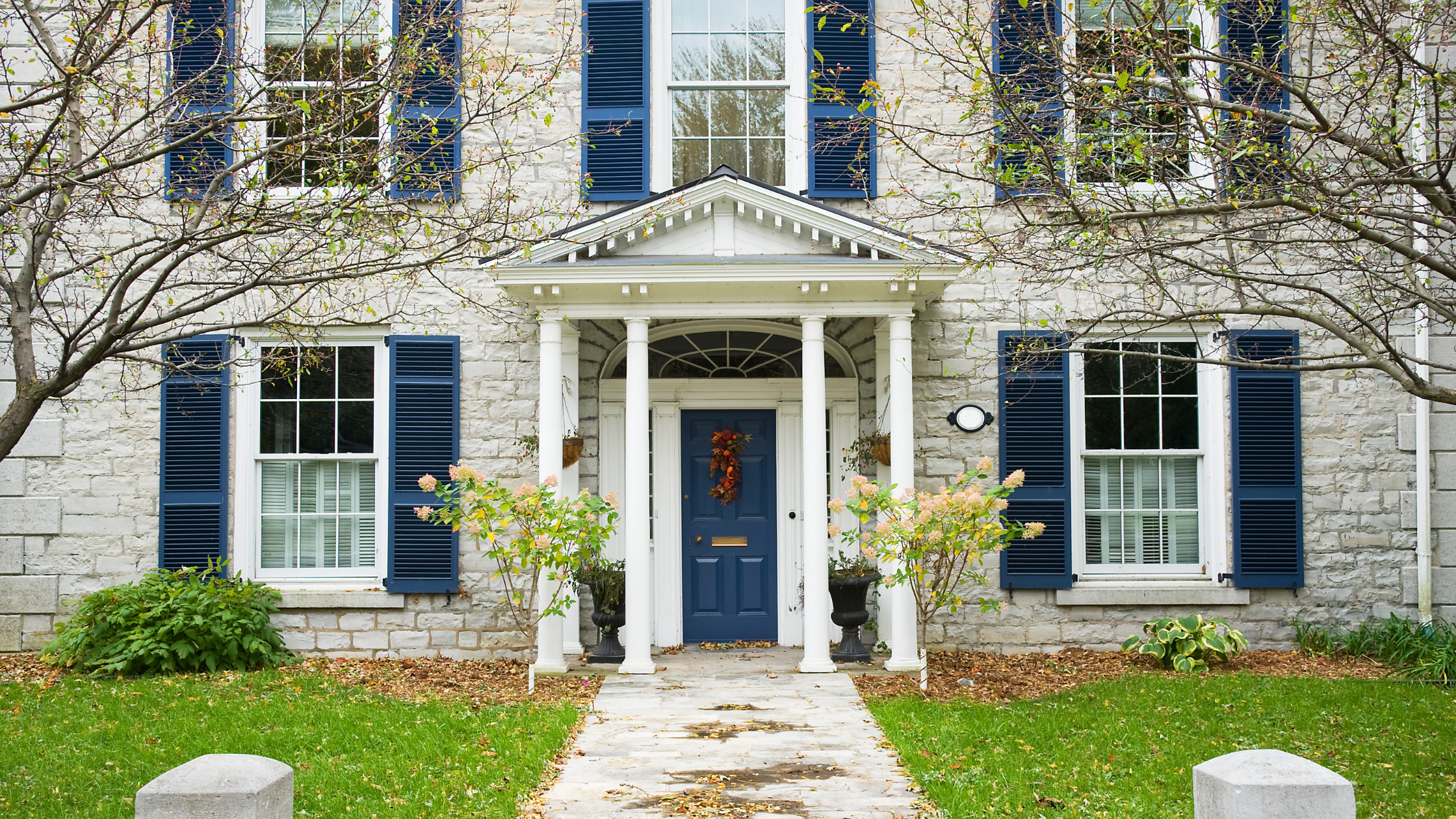 Large house with a blue front door and many windows with shutters on each.