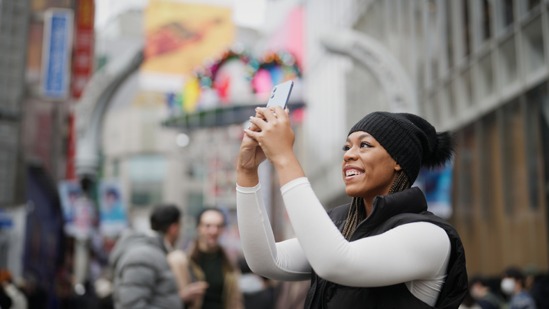 Happy young African American woman in a black cap snapping a photo of her surroundings. 