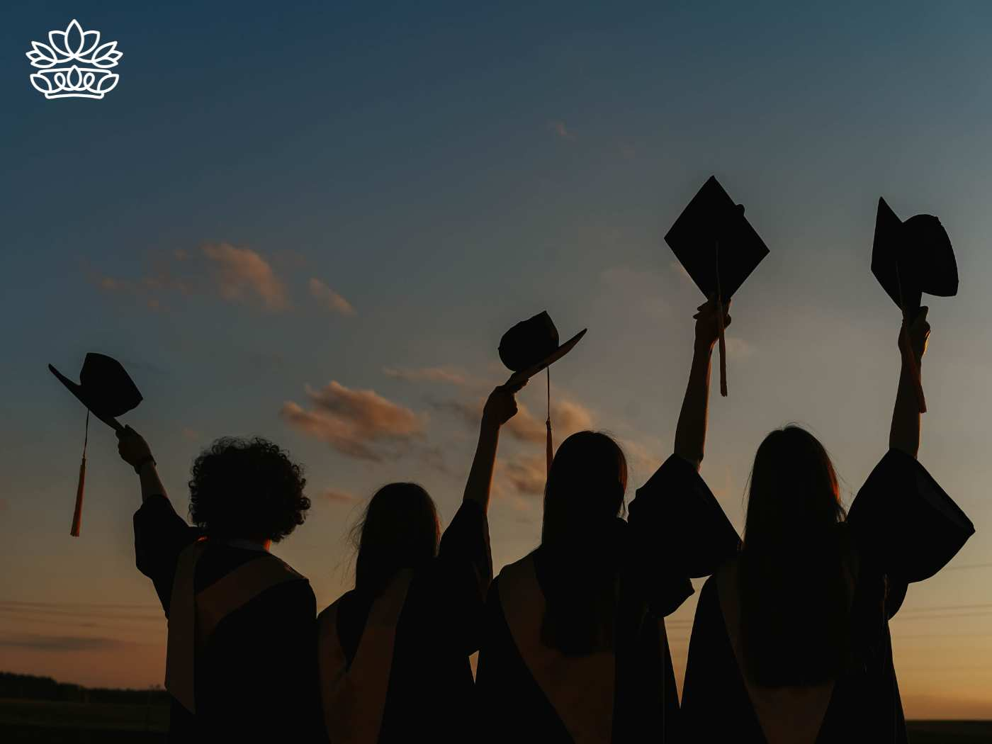 Silhouettes of graduates holding their mortarboards high against a vibrant sunset sky, symbolizing hope and achievement at the end of their academic journey. Graduation. Delivered with Heart. Fabulous Flowers and Gifts.