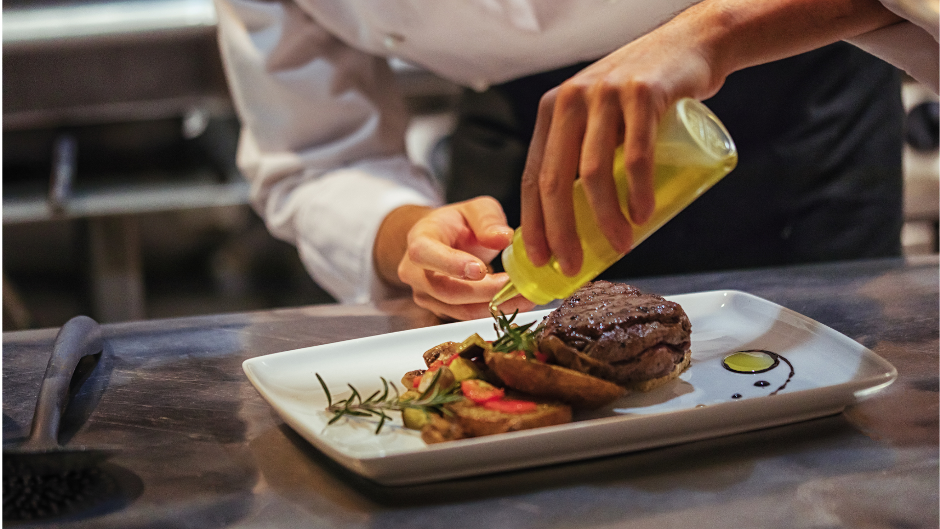 Gourmet chef plating a steak dish in a professional kitchen, drizzling olive oil over tender beef filet served with roasted vegetables, fresh rosemary, and artistic sauce decoration on a white rectangular plate. Fine dining restaurant plating and presentation for culinary excellence.