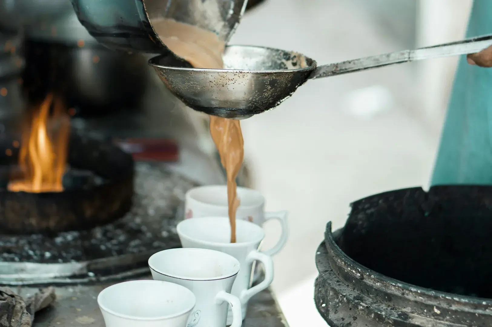 Straining hot milk tea into white ceramic cups.
