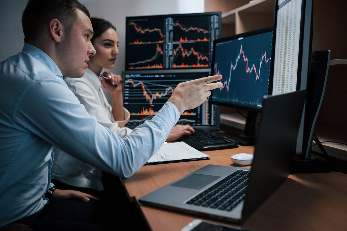 Business analysts reviewing charts and data on multiple screens during a business acquisition process