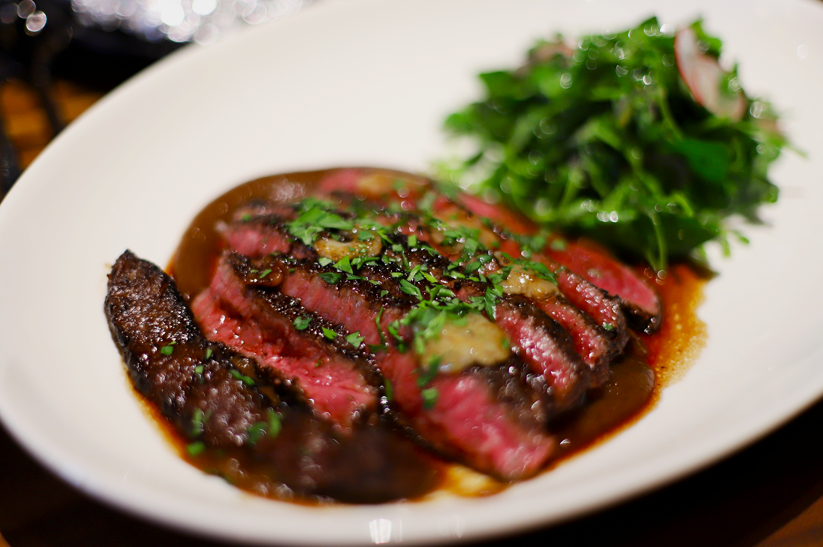 A plate of medium-rare sliced steak garnished with herbs and served with a fresh green salad. The dish exudes a savory and appetizing allure.