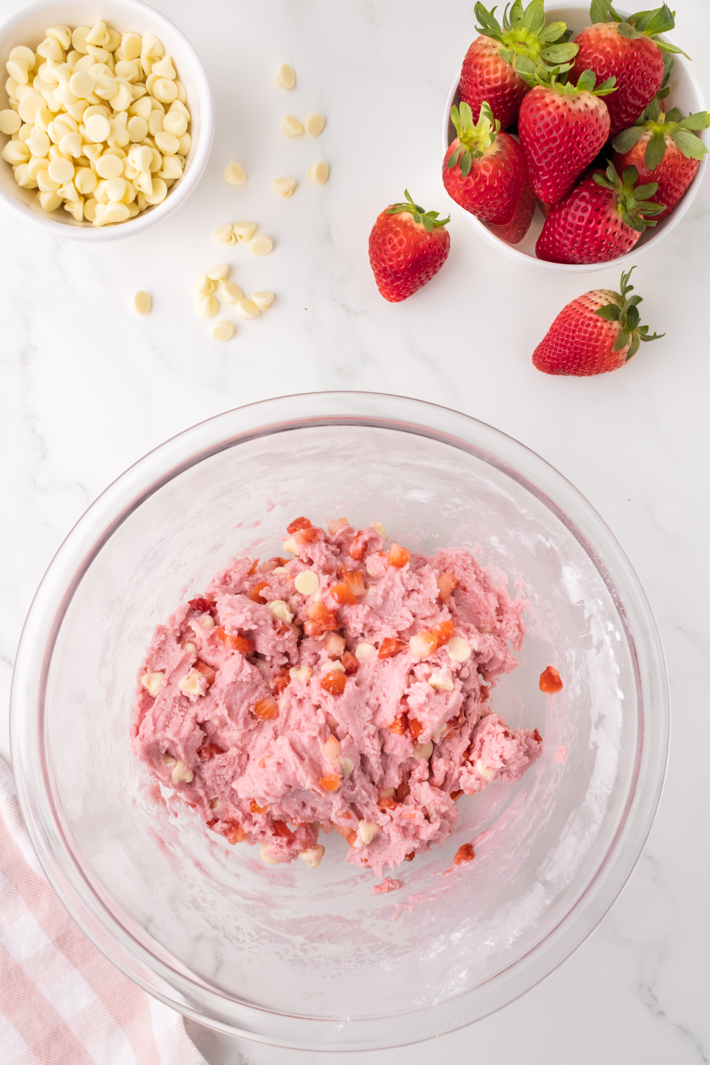 diced strawberries and white chocolate chips stirred into pink cookie dough in large bowl