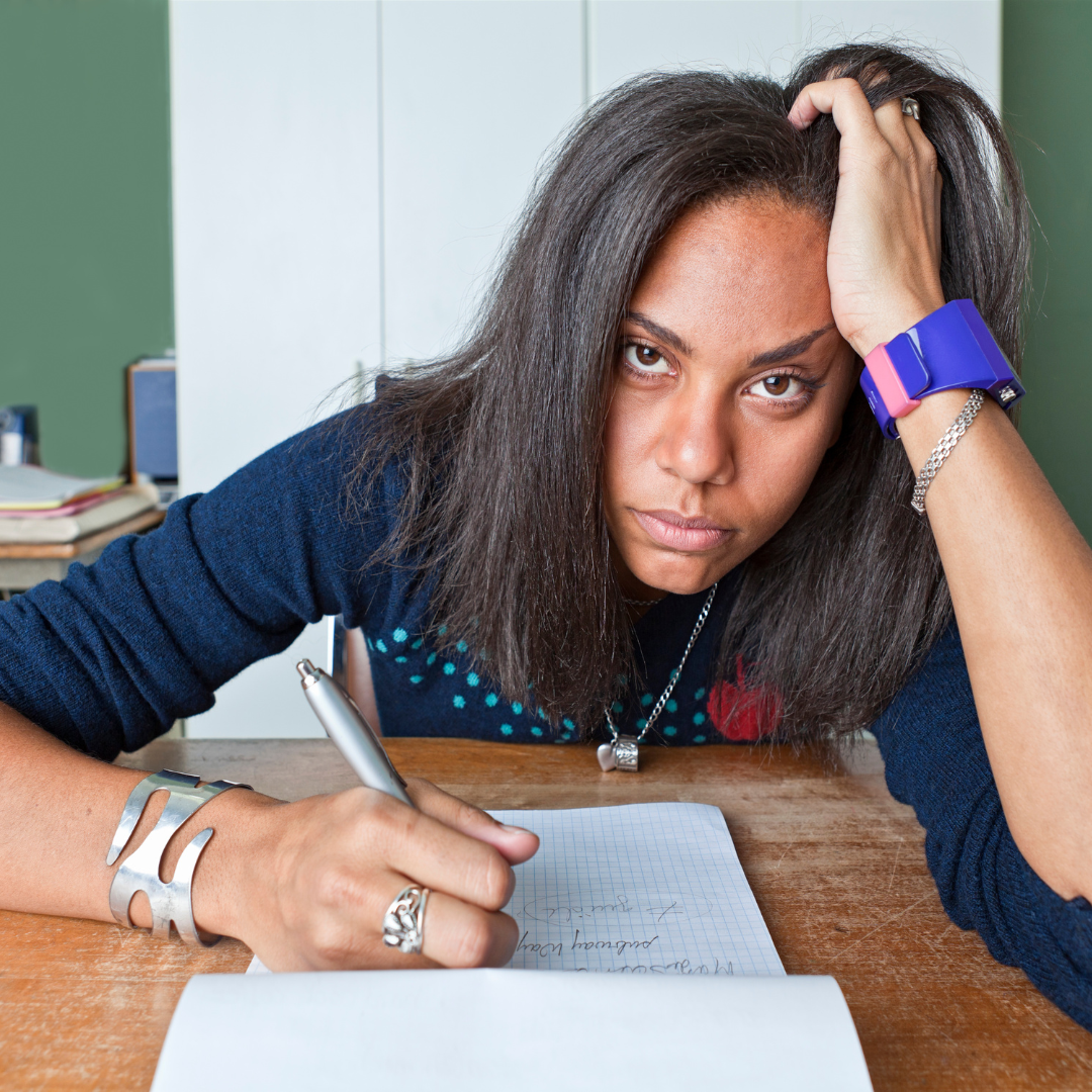 A young woman with a large purple watch looks annoyed and tired as she writes on a notepad.
