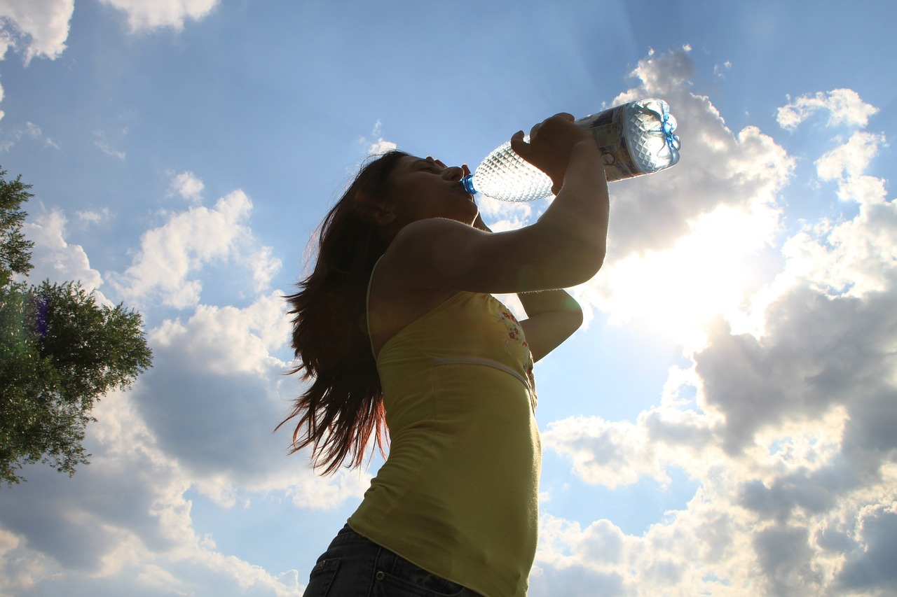 An image of a woman oudoors drinking a bottle of water. 