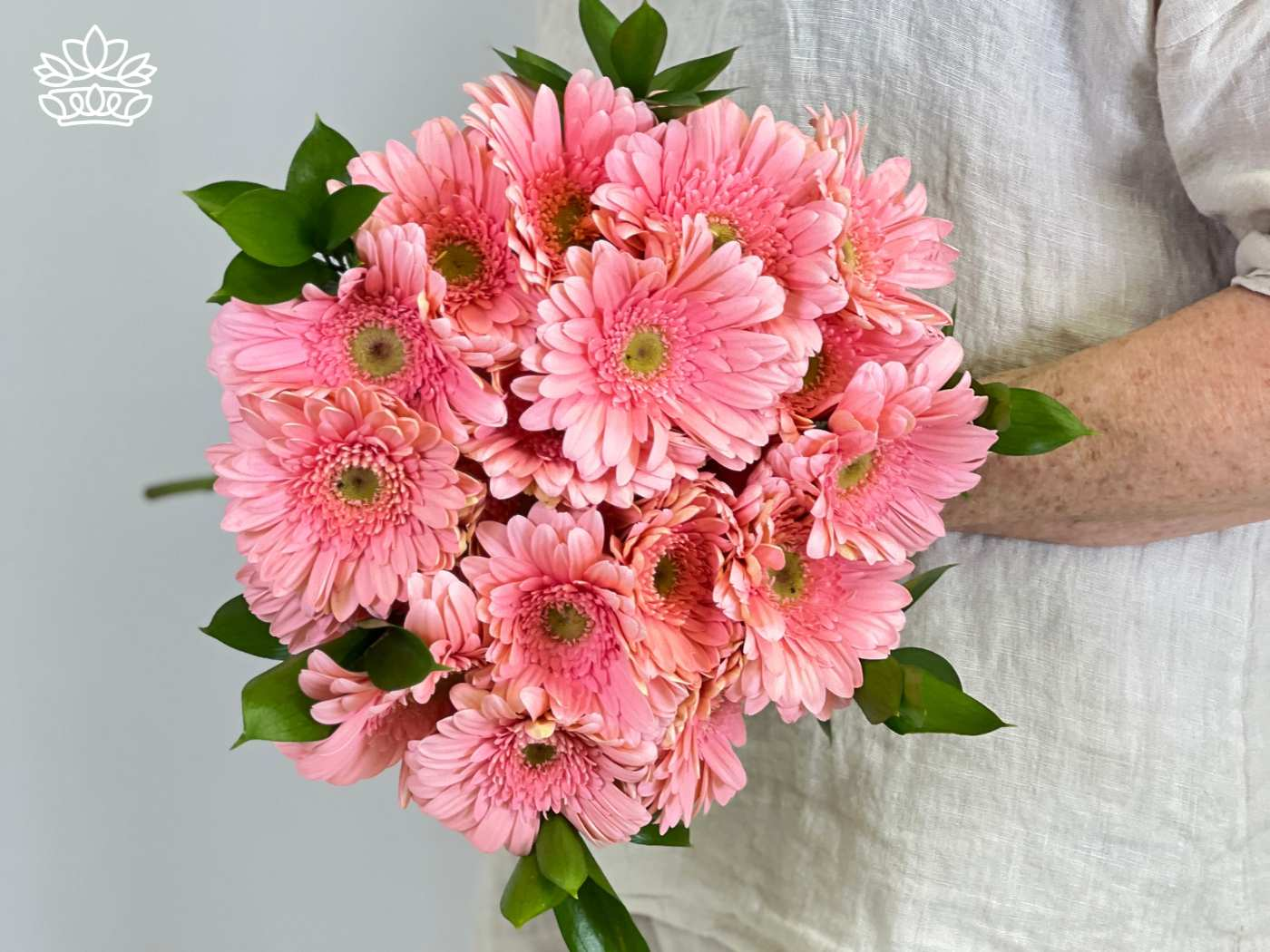 A soft pink bouquet of Gerbera daisies, held with care and accompanied by green leaves. Fabulous Flowers and Gifts. Gerberas Collection. Delivered with Heart.