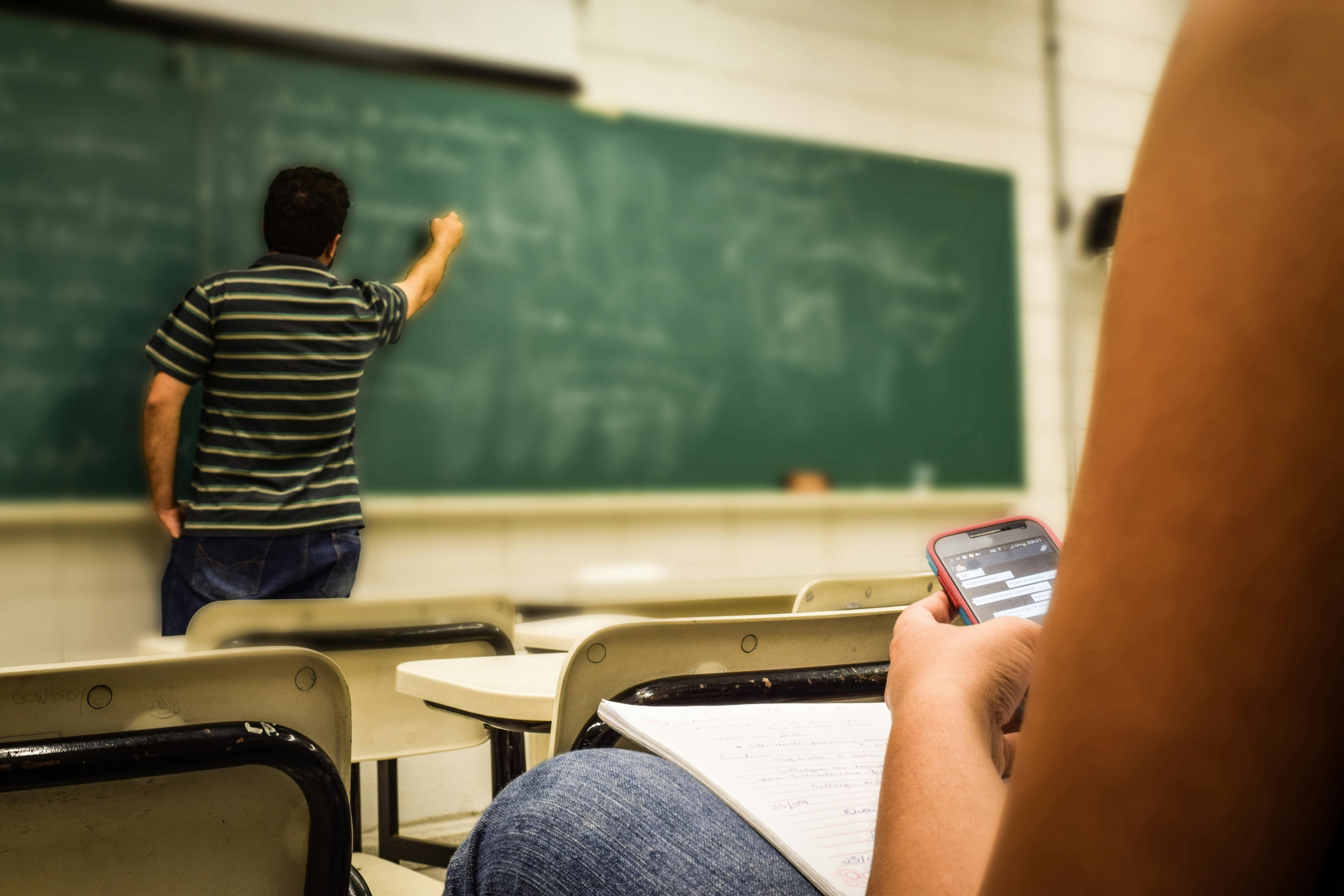 Student texting while the teacher is writing on the blackboard