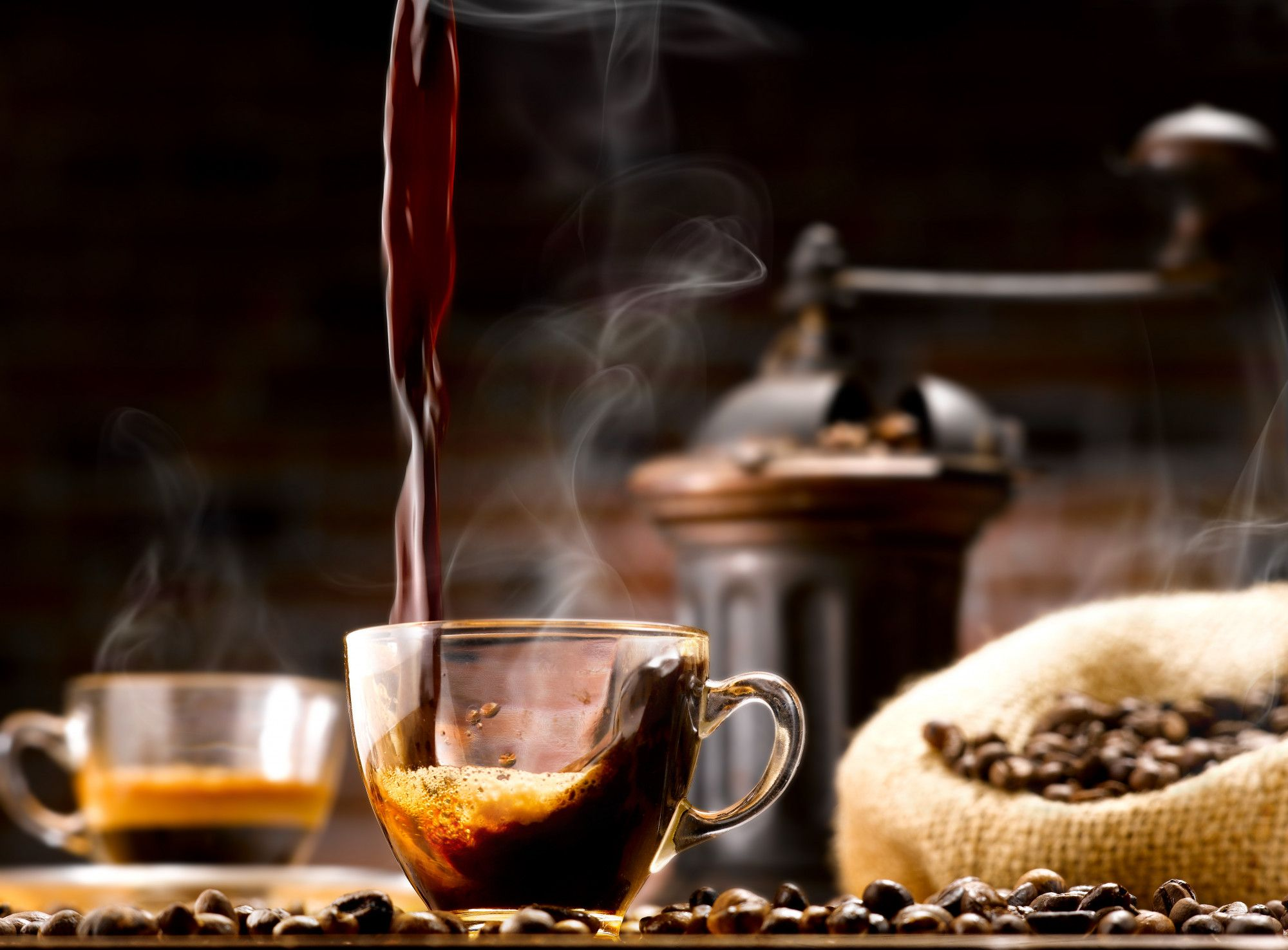 Pouring of a dark roast brewed coffee into a glass coffee glass with french press and with a dark roast type of coffee beans