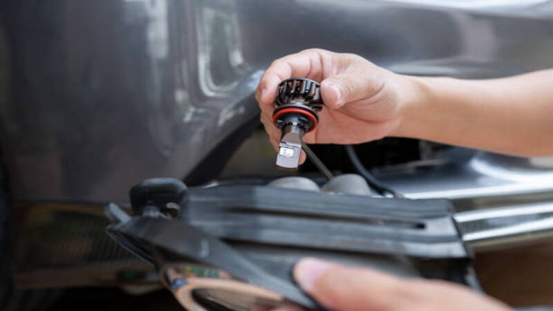 A mechanic removing the damaged headlight bulb of a car.