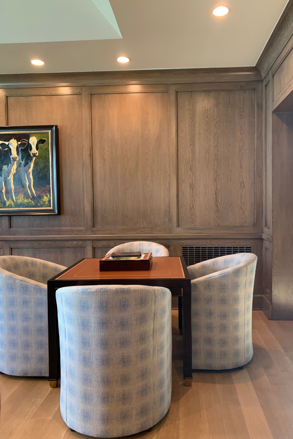 a painting of cows hangs to the left of a card table with club chairs