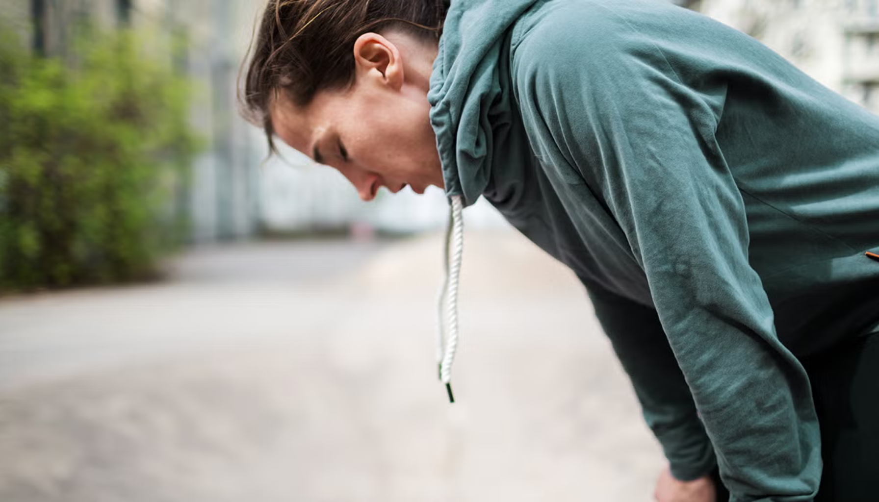 Kvinne bøyer seg frem og puster tungt etter fysisk aktivitet, viser tegn på utmattelse eller pustevansker.