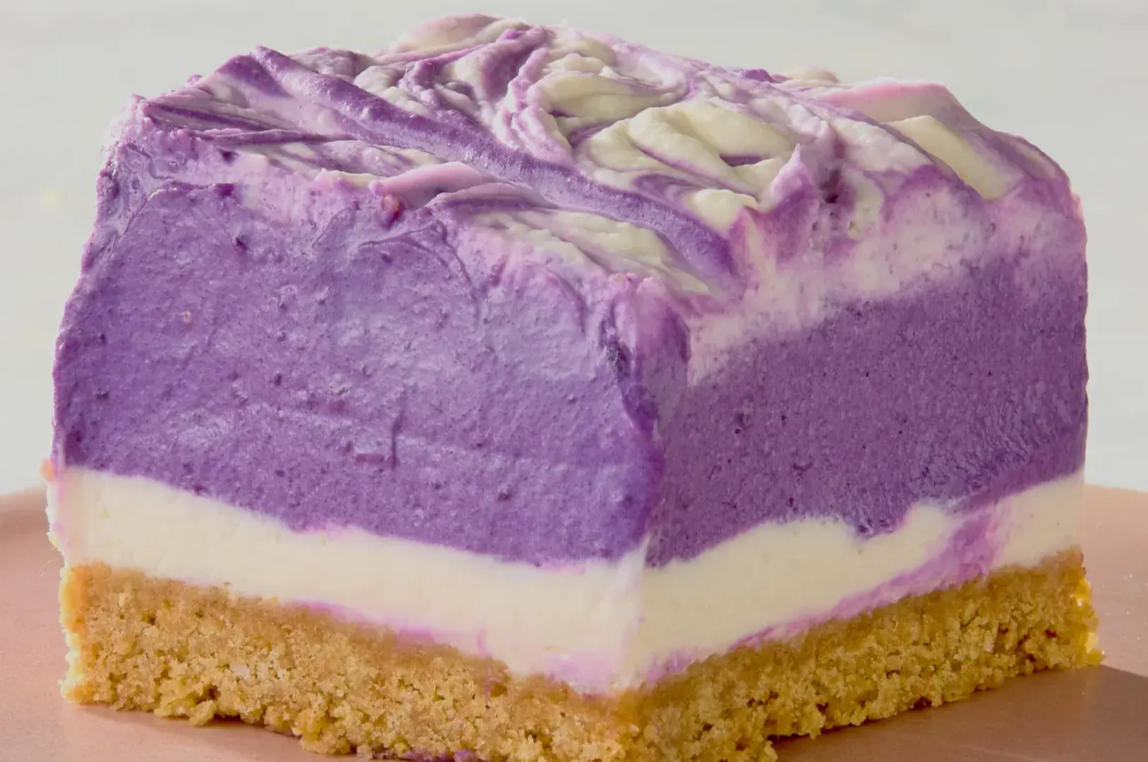 A slice of purple layered dessert with a crumbly base, showing a gradient of purple and white colors.