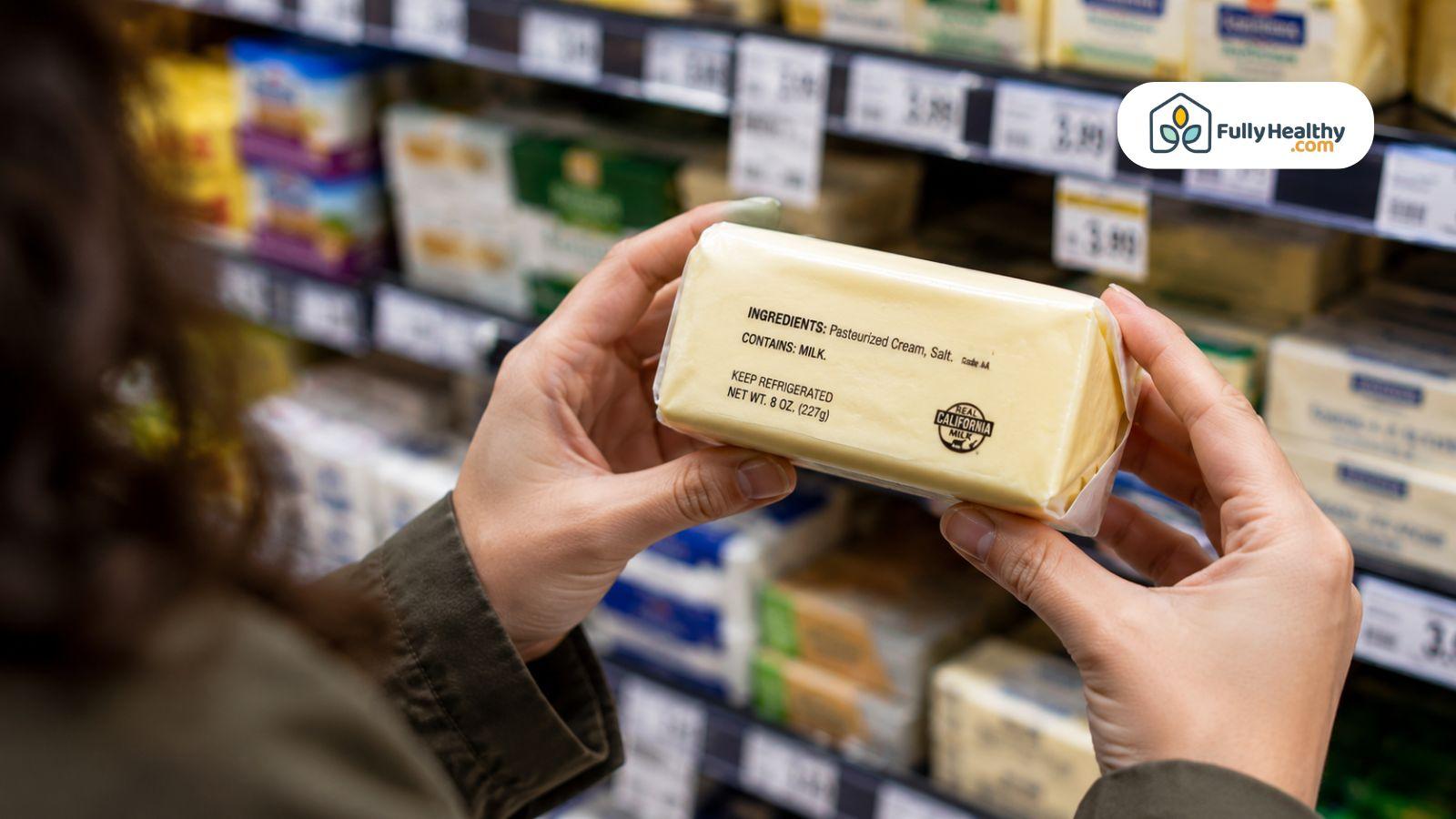 Shopper reading butter ingredient label carefully inside bright supermarket dairy aisle today.