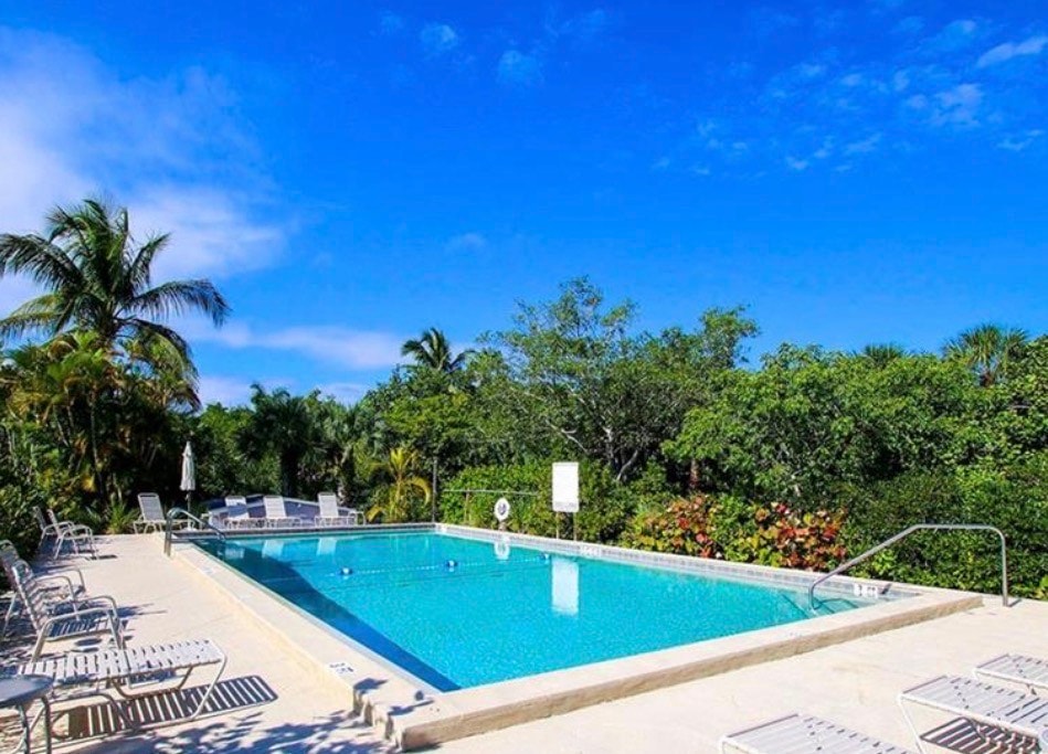 The image depicts a luxurious community pool area featuring a hot tub, surrounded by lush tropical landscaping and tall palm trees, creating a serene atmosphere. This inviting space is part of the Gulf Pines community on Sanibel Island, known for its private beach access and exceptional near beach estates.