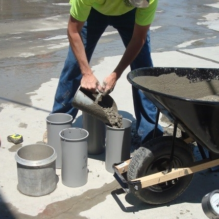 A technician pouring freshly mixed concrete into a cylinder mold