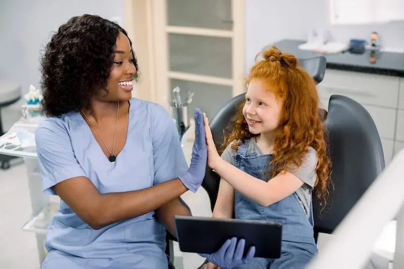 A dentist or dental hygienist giving a high-five to a smiling young girl in a dental clinic.