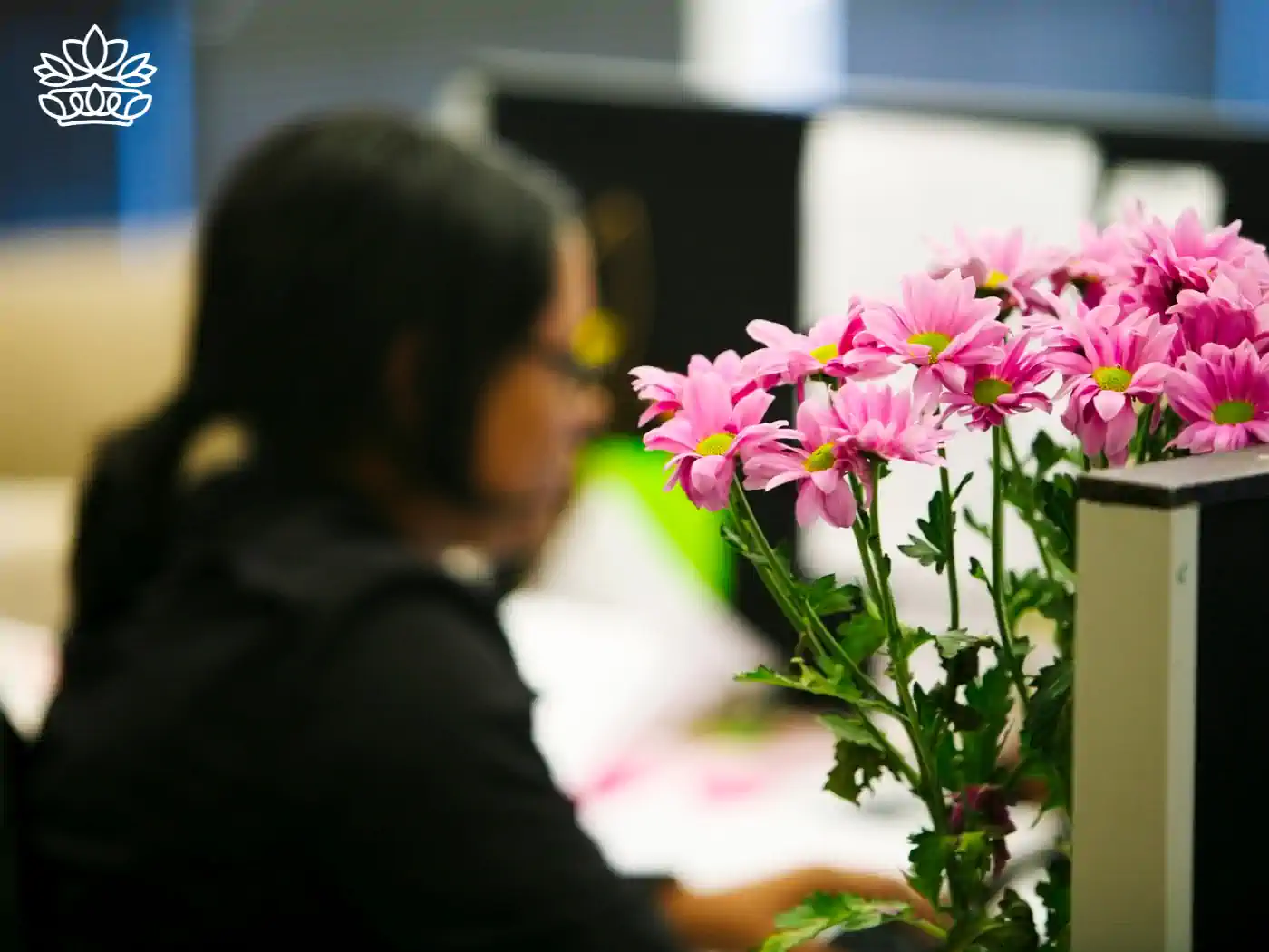 Close-up of a bouquet of pink flowers on an office desk with a blurred background of a woman working. Fabulous Flowers and Gifts, Office Collection.